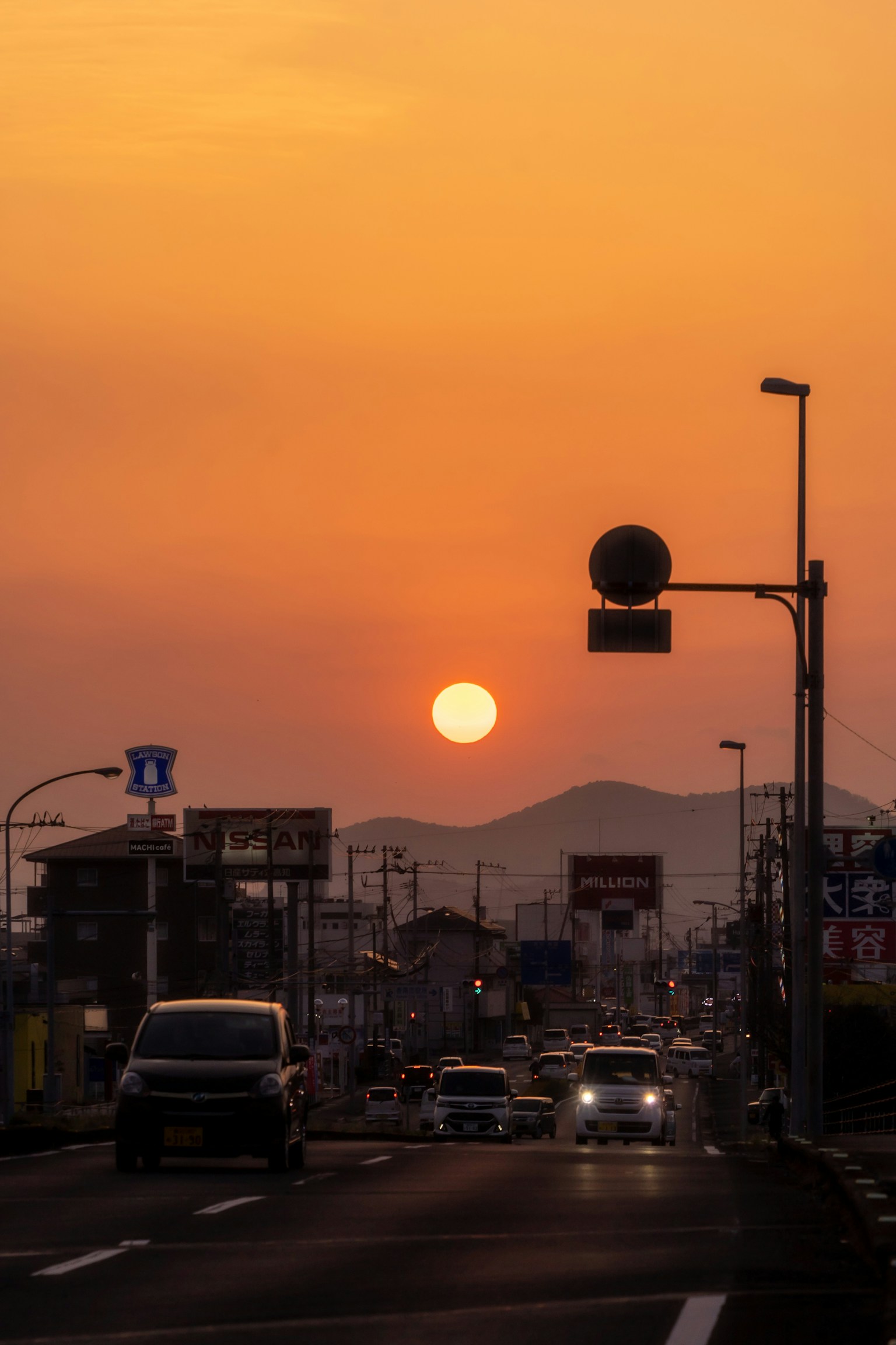 Cityscape at sunset with an orange sun and cars on the road