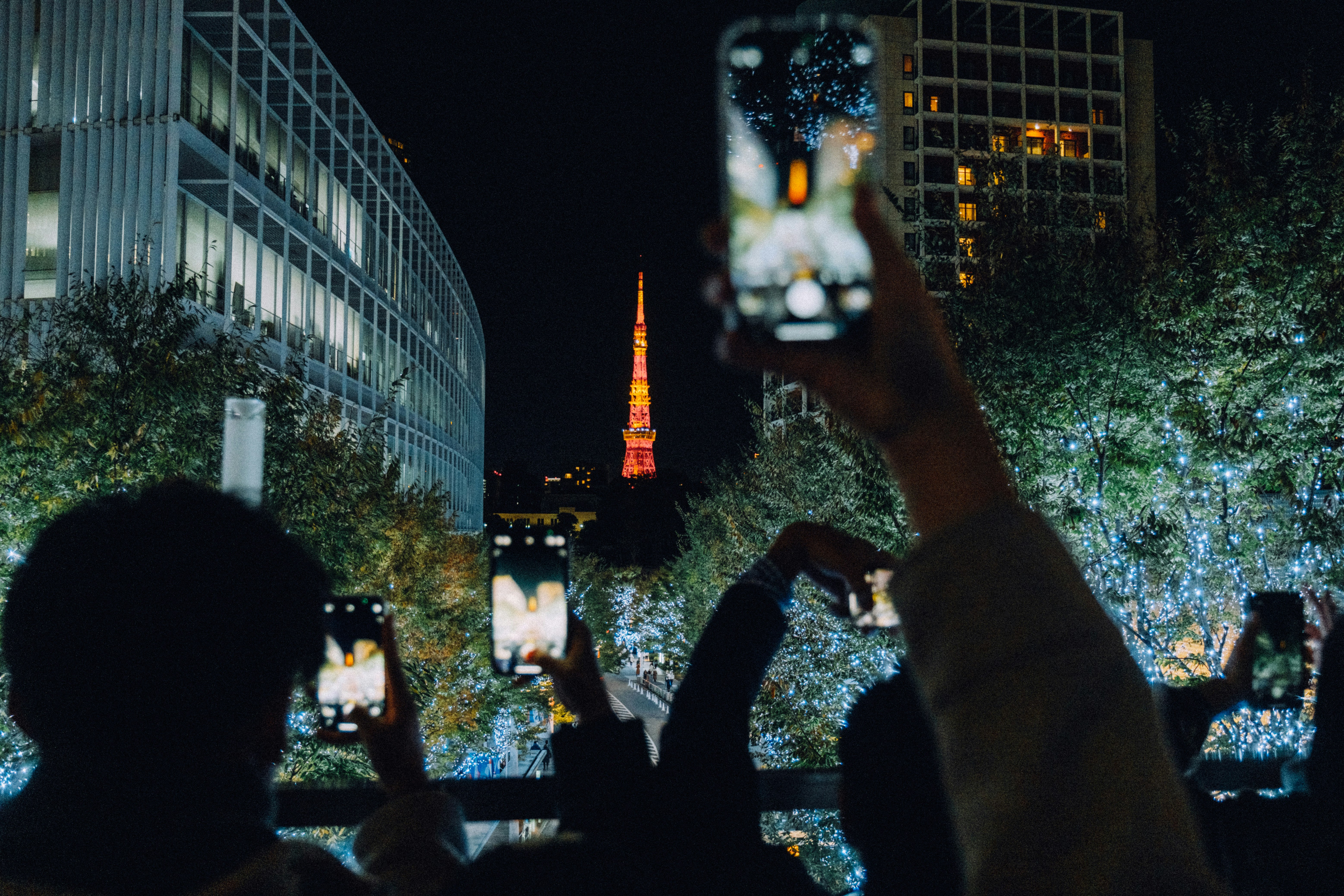 東京タワーを背景にした夜の風景でスマートフォンを持つ人々