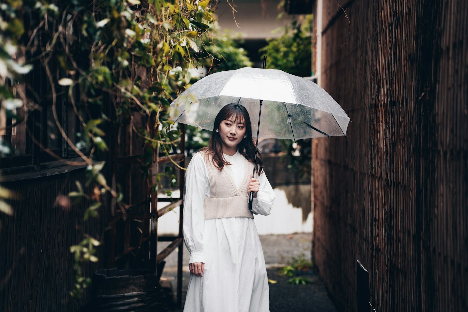 穿着白色连衣裙的女人在狭窄的小路上拿着透明伞