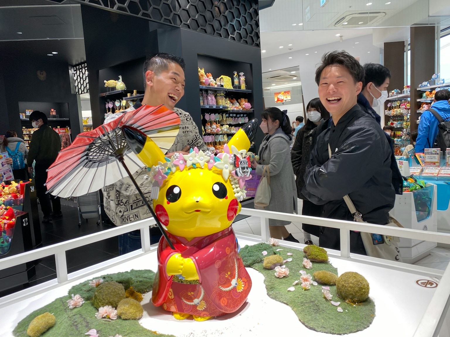 Patung Pikachu yang mengenakan kimono dengan orang-orang tersenyum di toko