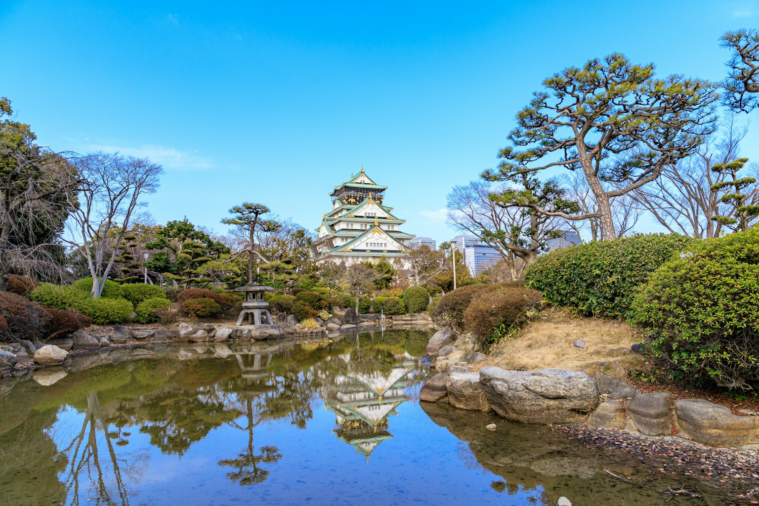 大阪城的风景在宁静的池塘中倒影，周围环绕着郁郁葱葱的绿植