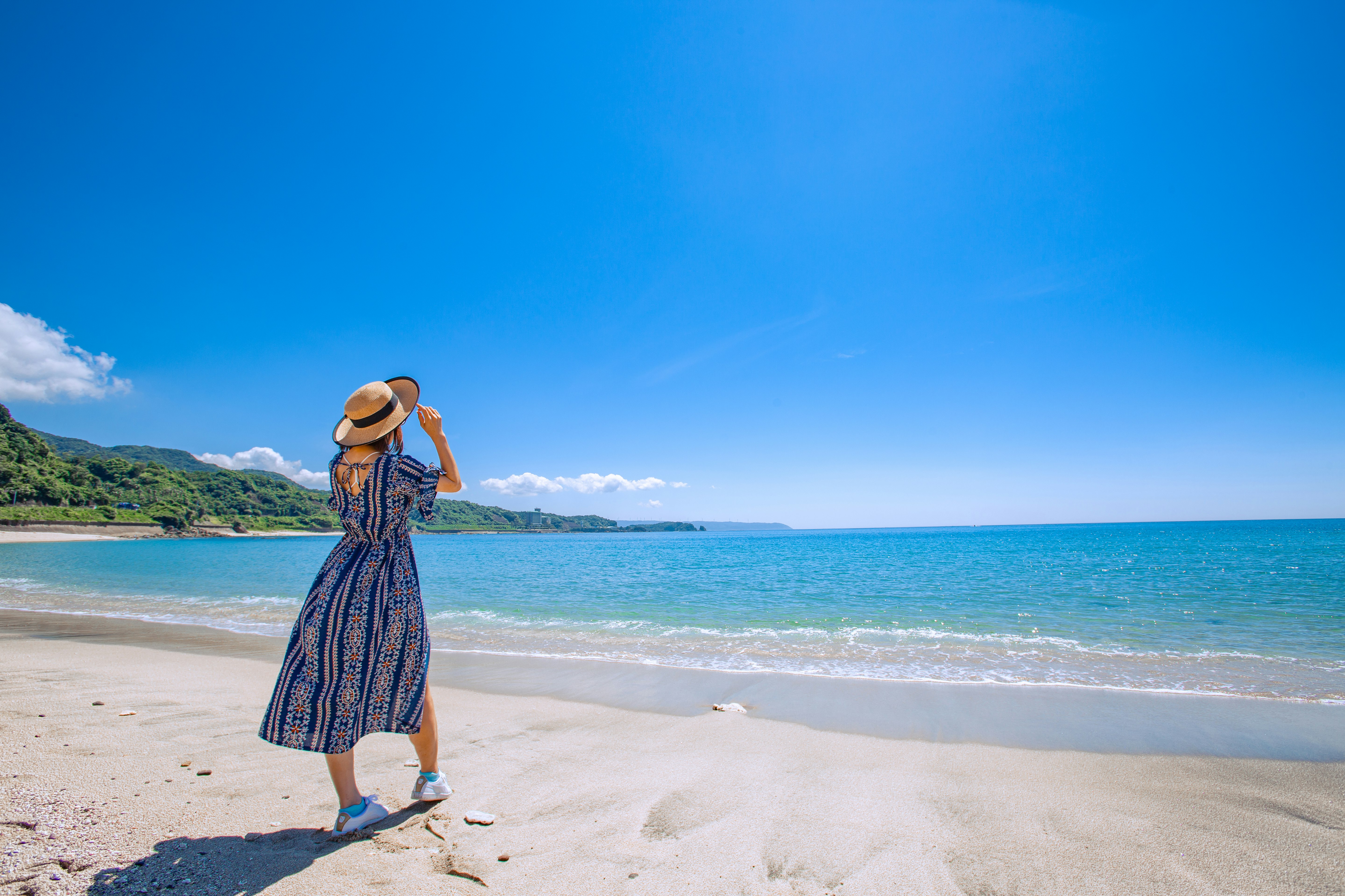 mujer con sombrero de paja sentada en una playa de arena junto al océano