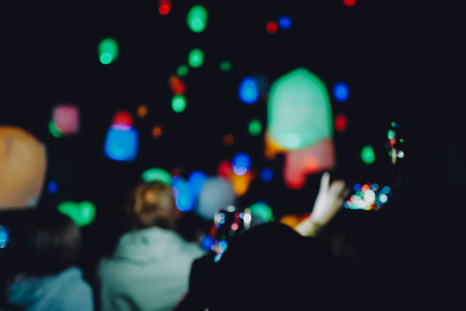 People looking up at colorful lanterns floating in the night sky
