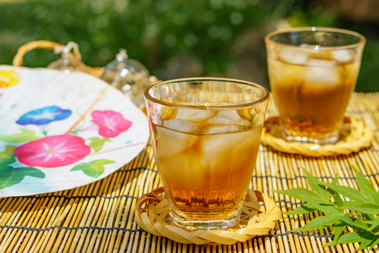 Two glasses of iced tea on a bamboo mat with a floral plate
