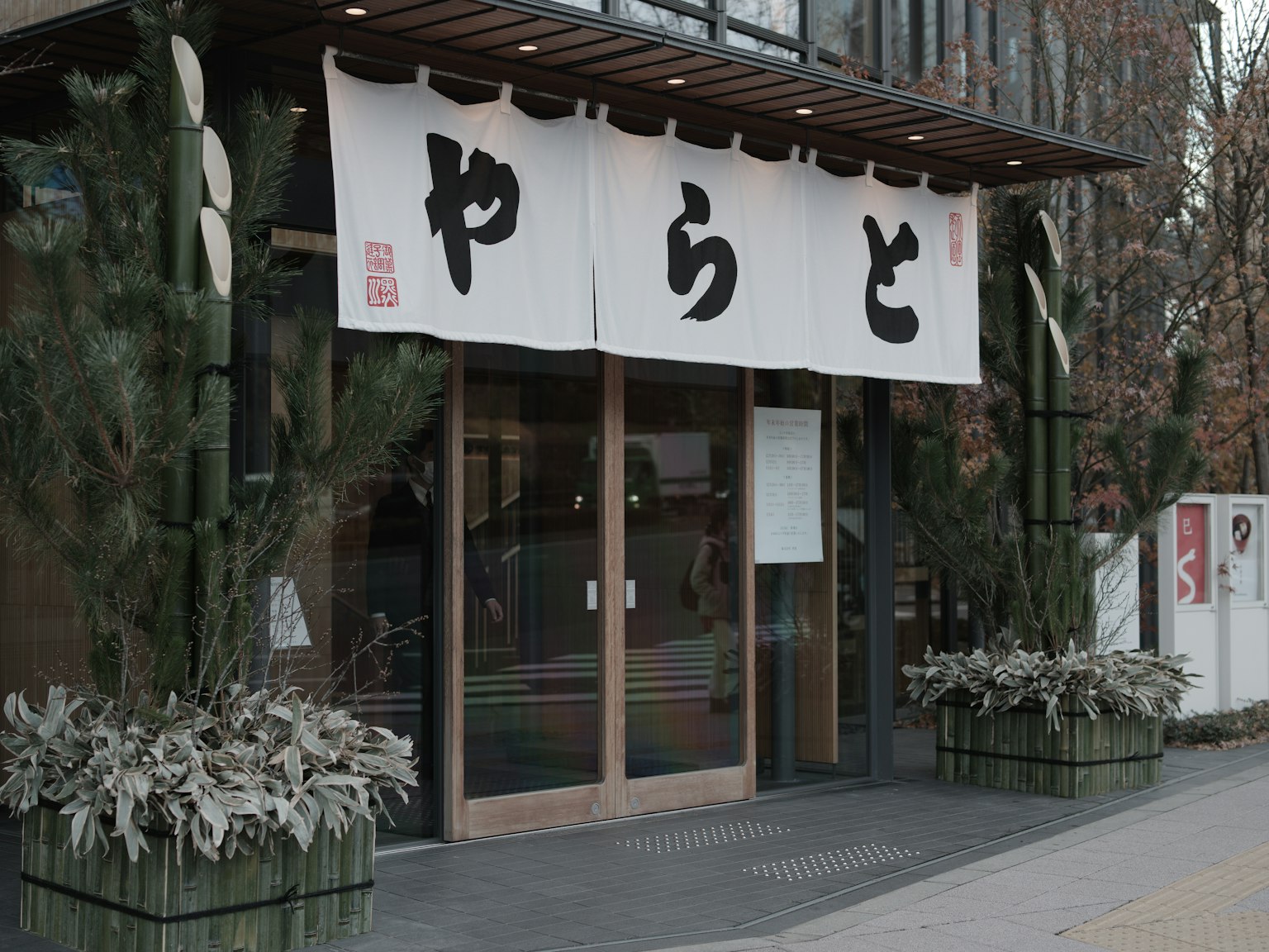 Masuk restoran Jepang dengan noren putih dan tanaman hijau