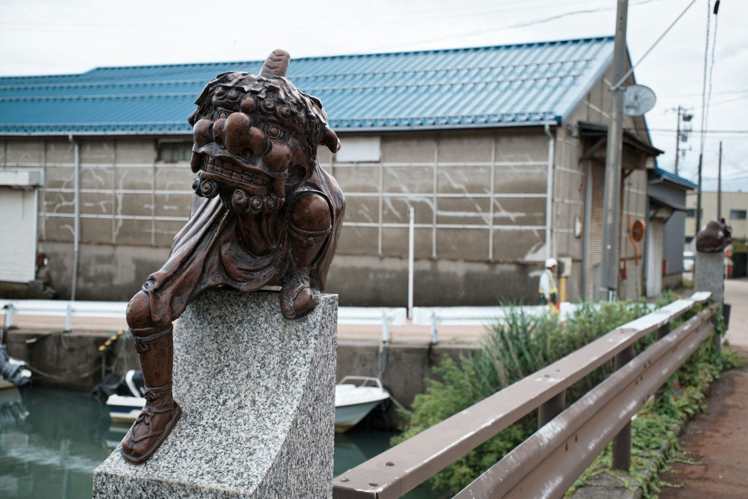 Sculpture of a figure with a lion-like head near a blue-roofed building