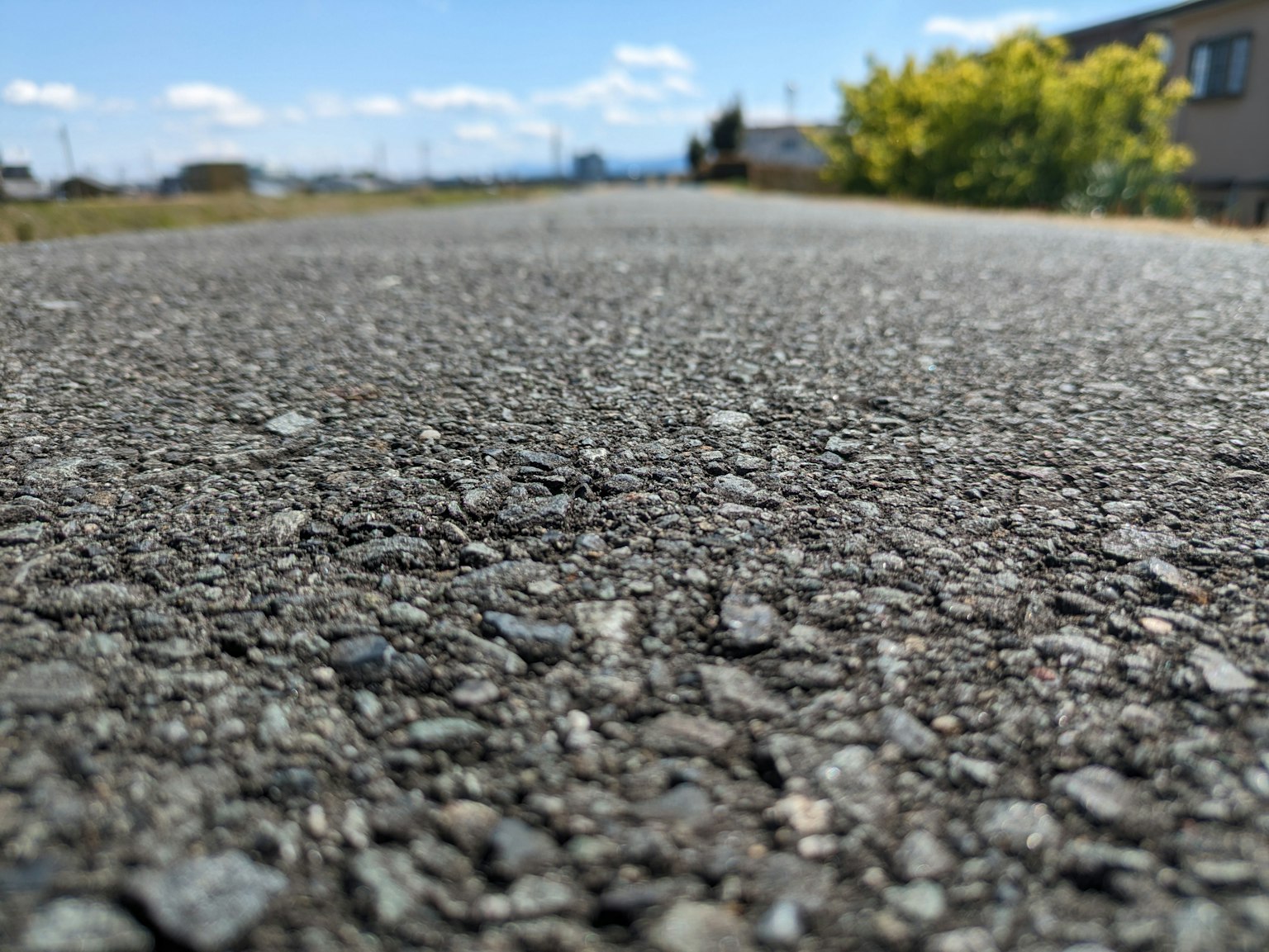 Close-up jalan aspal dengan langit biru dan tanaman hijau di latar belakang