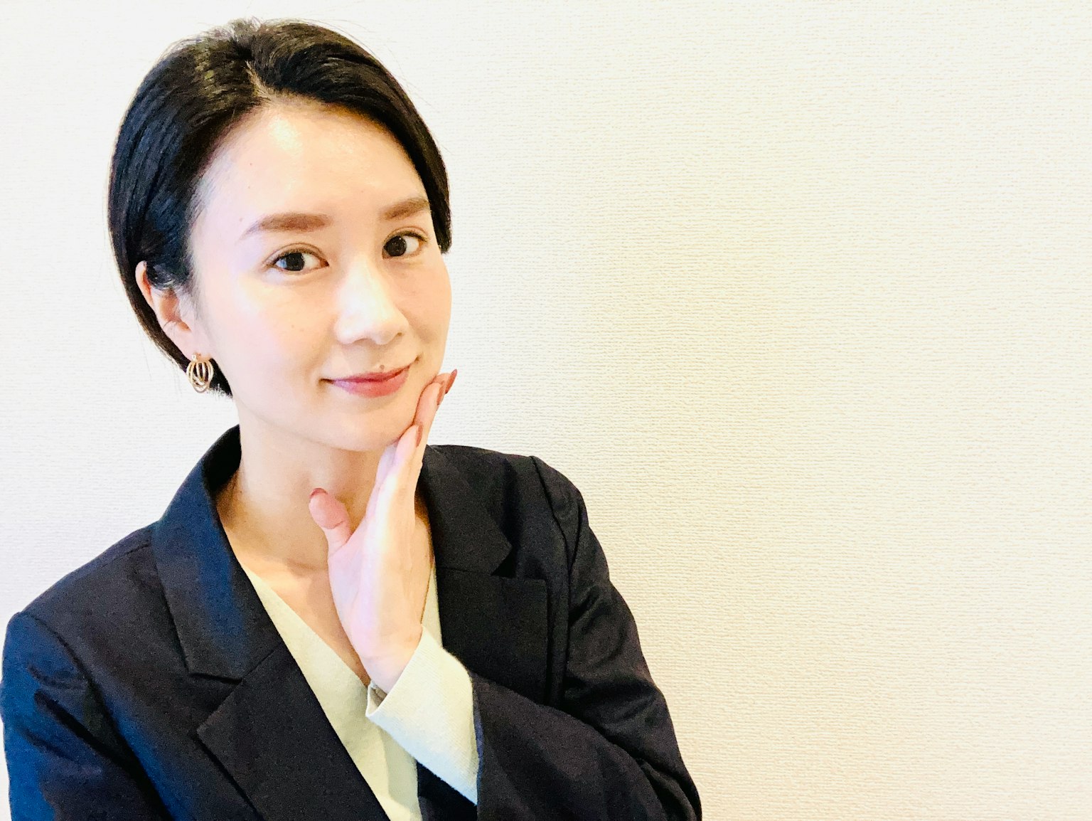 一位穿着商务套装的女性微笑着，手放在下巴上