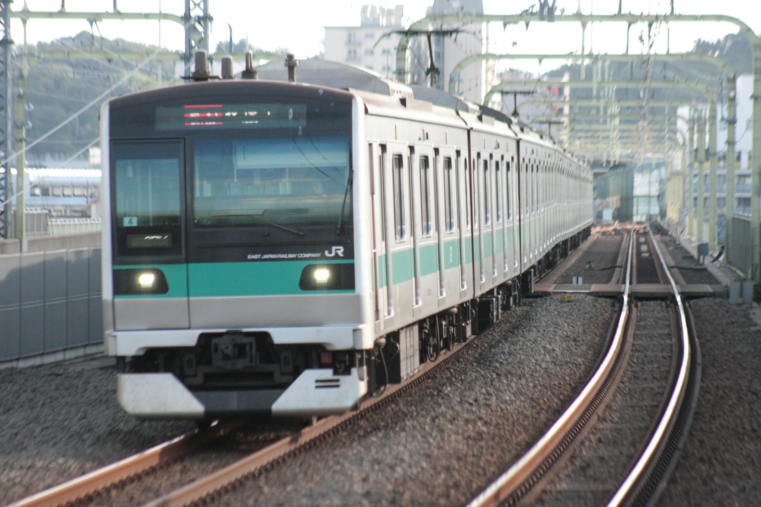 Treno argento con striscia verde che curva sui binari