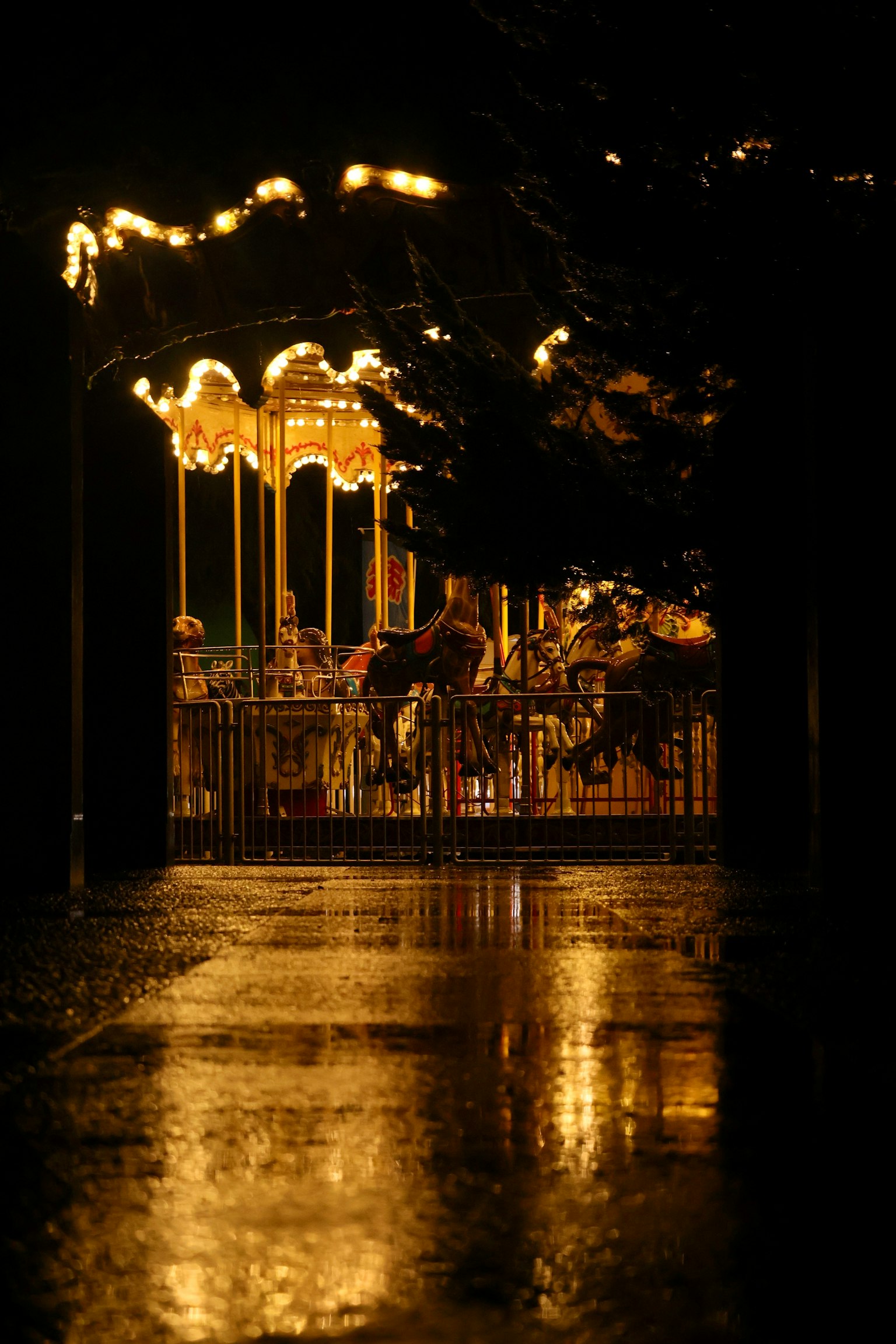 Carrusel iluminado en un parque de atracciones por la noche con reflejos en el pavimento mojado