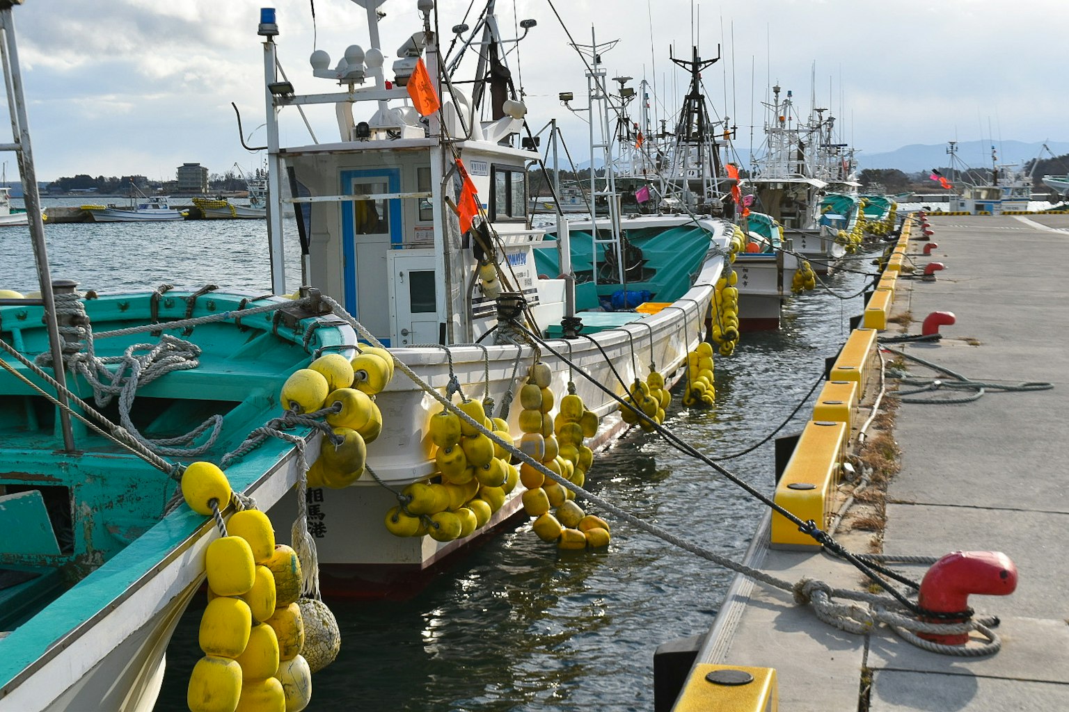 Barche da pesca ormeggiate in un porto con boe gialle appese alle imbarcazioni