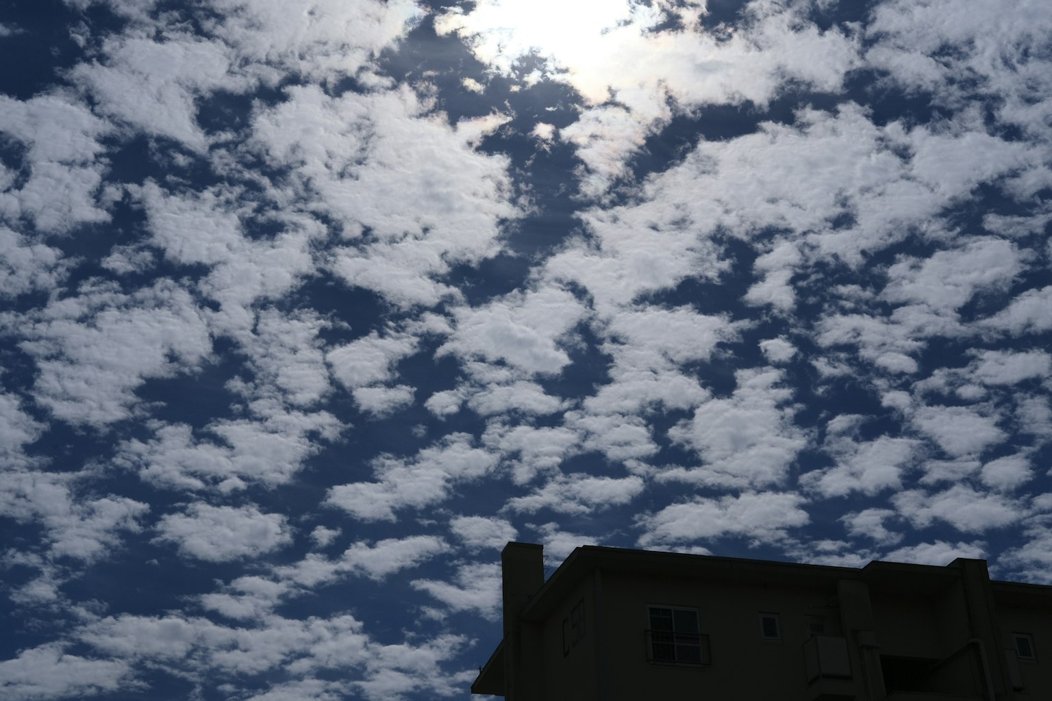 Cielo azul brillante lleno de nubes blancas y silueta de un edificio