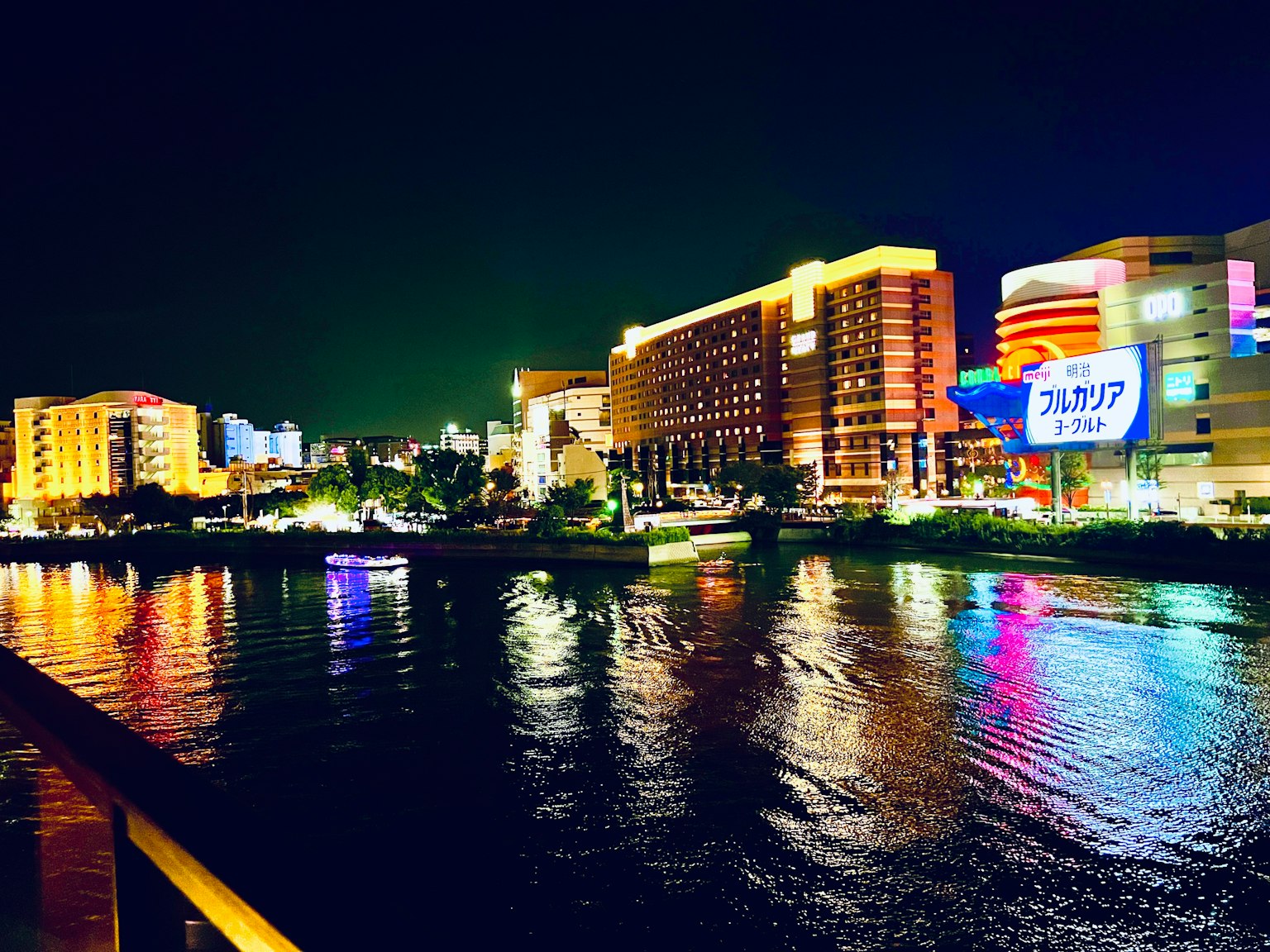 夜間沿河的城市景觀，建築物燈光閃爍，色彩斑斕的倒影