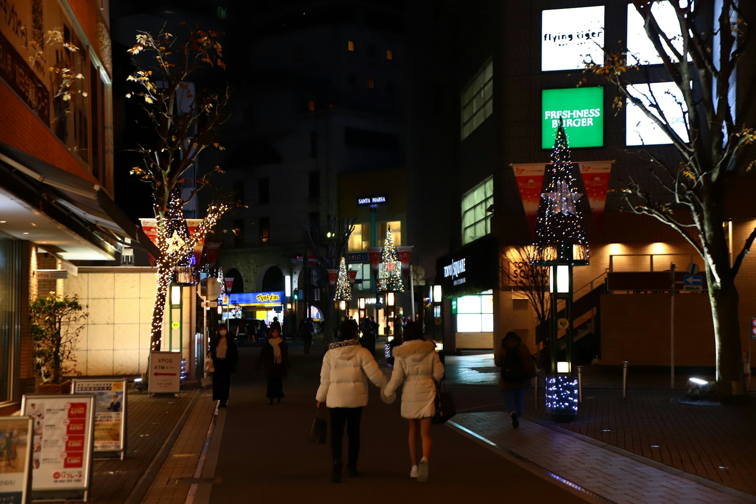 夜晚街道上行走的情侣，树木和商店被照亮