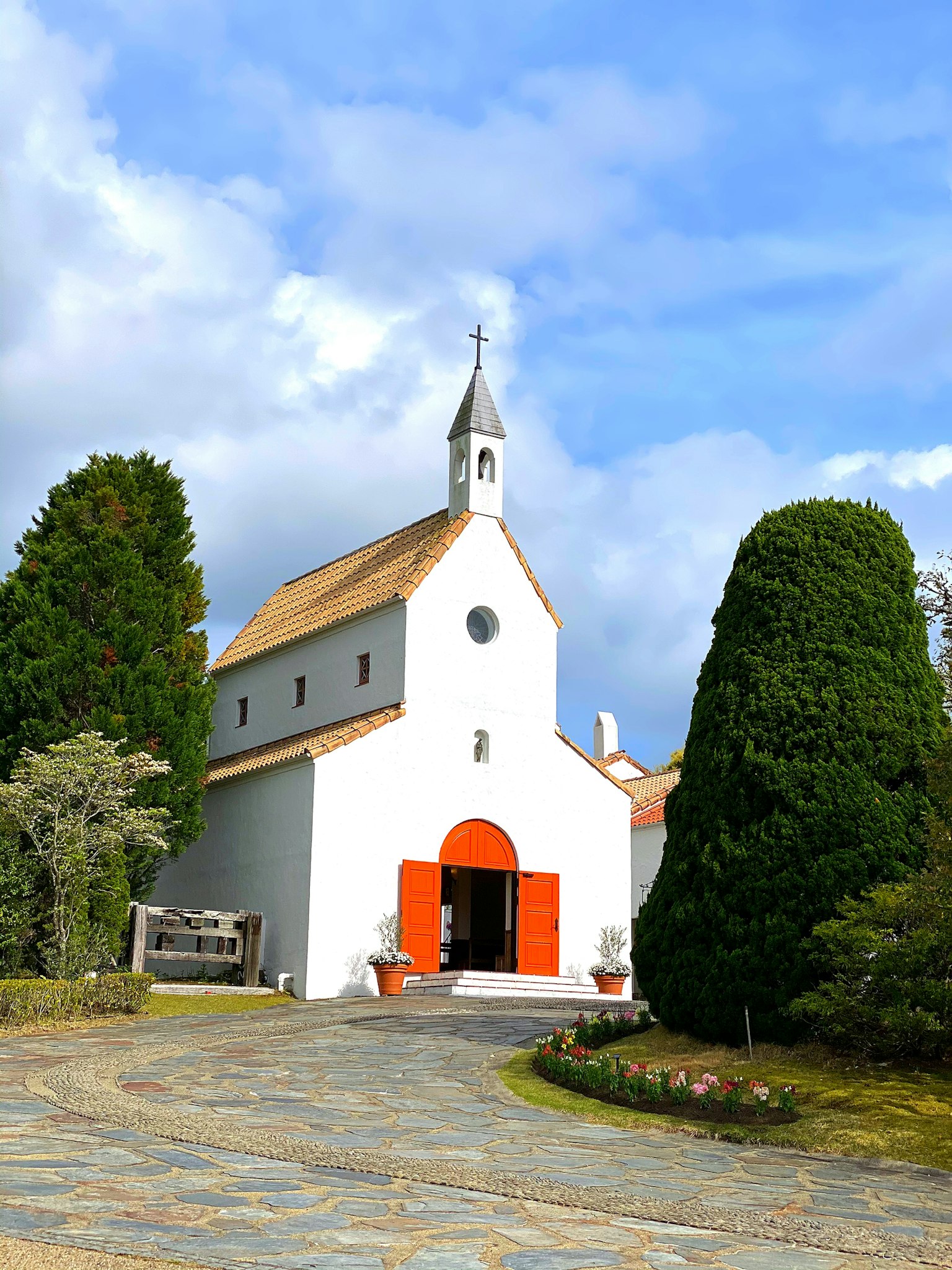 Chiesa bianca con porte arancioni circondata da alberi verdi e cielo blu