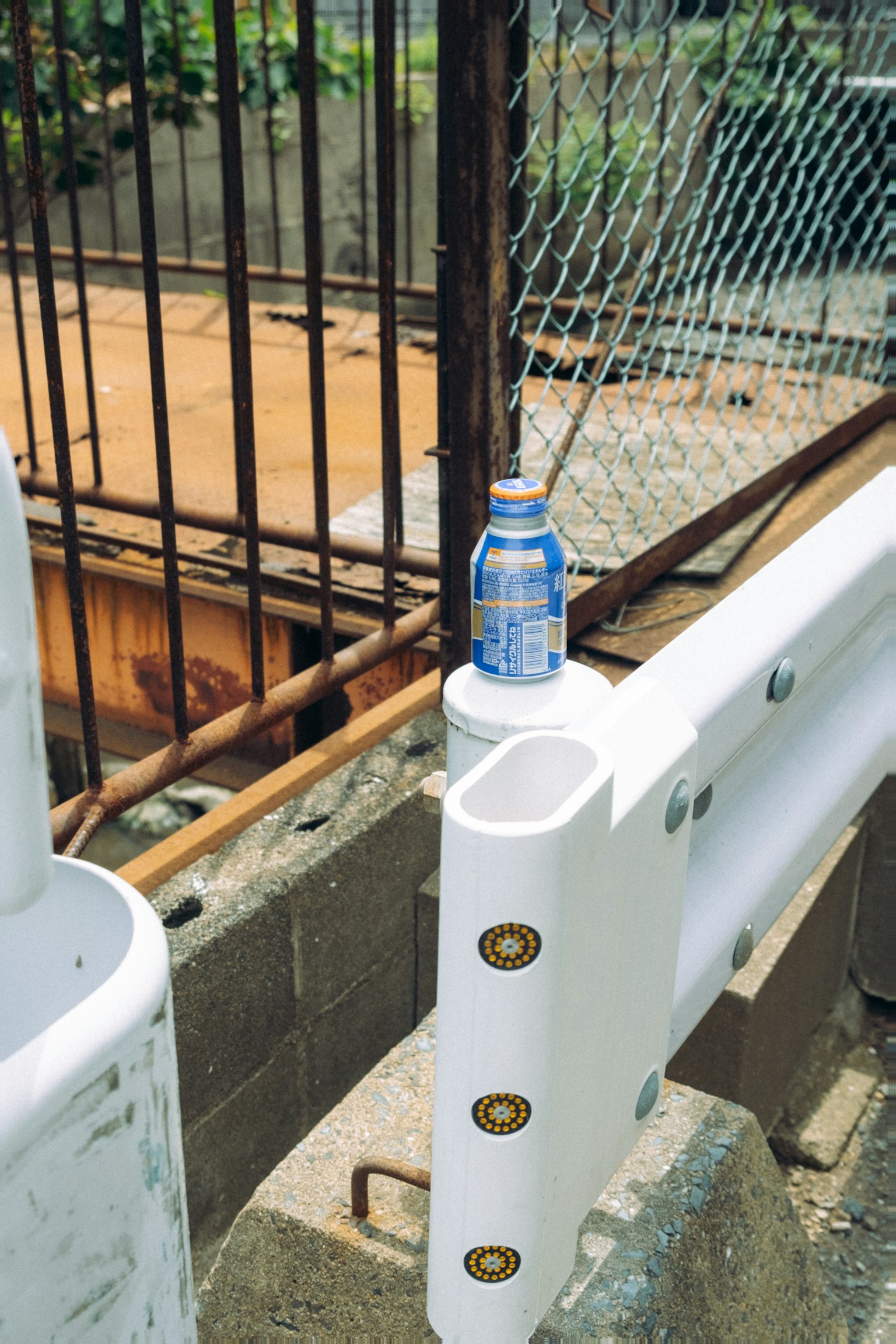 Eine blaue Flasche auf einer weißen Barriere mit einem rostigen Eisenzaun im Hintergrund