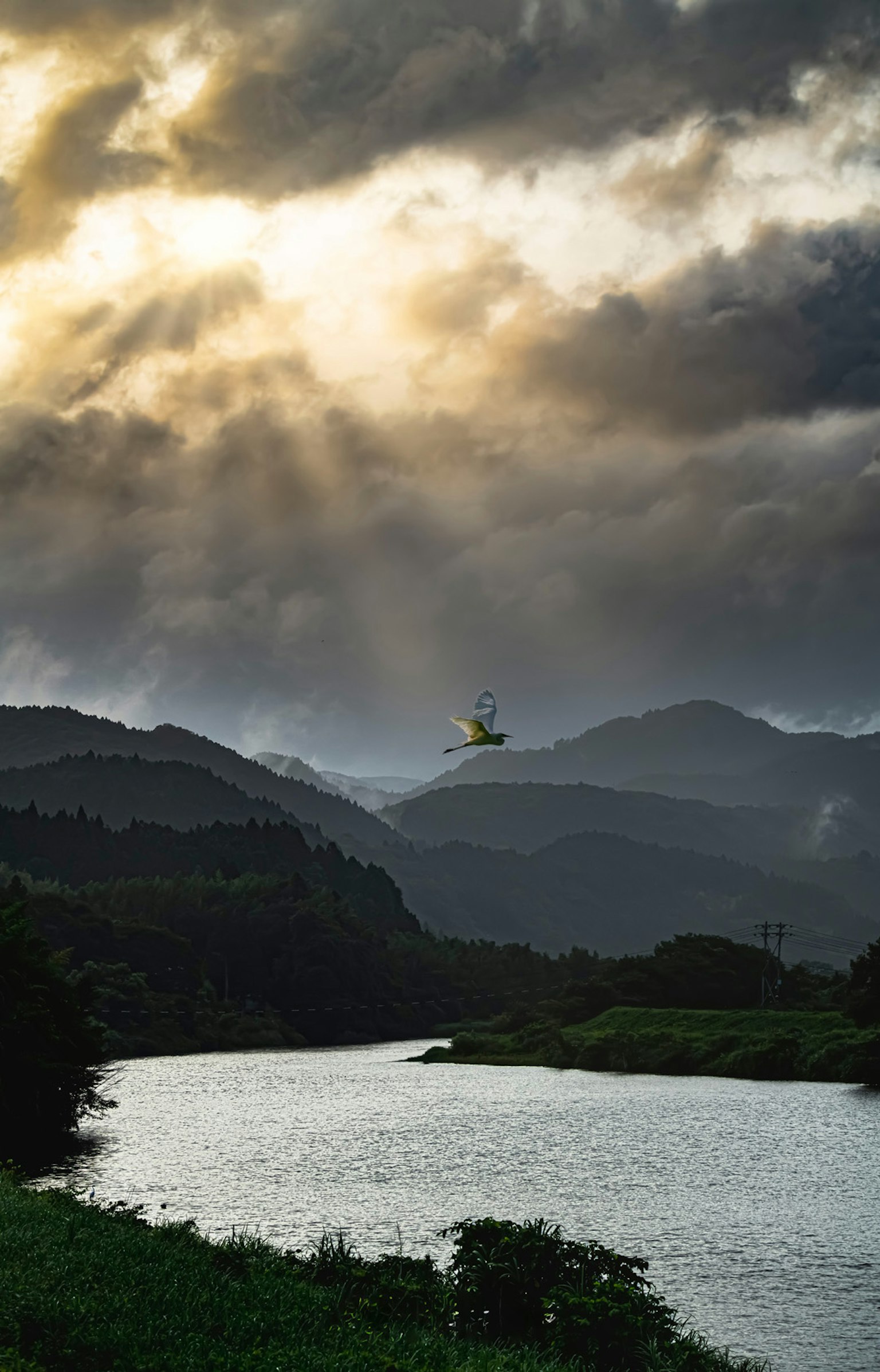 Malersiche Aussicht auf Berge mit Sonnenlicht, das durch Wolken über einem Fluss bricht