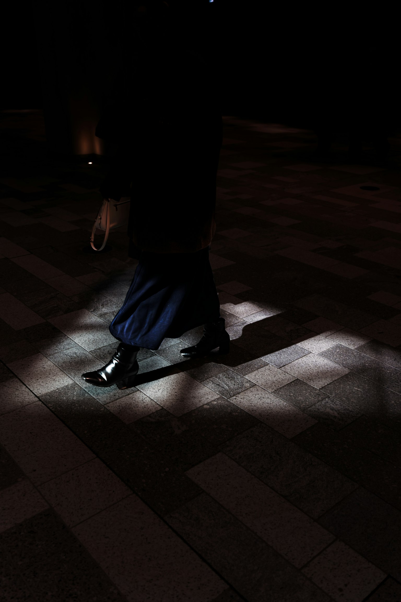 Persona che cammina in uno spazio scuro illuminato da una luce sul pavimento