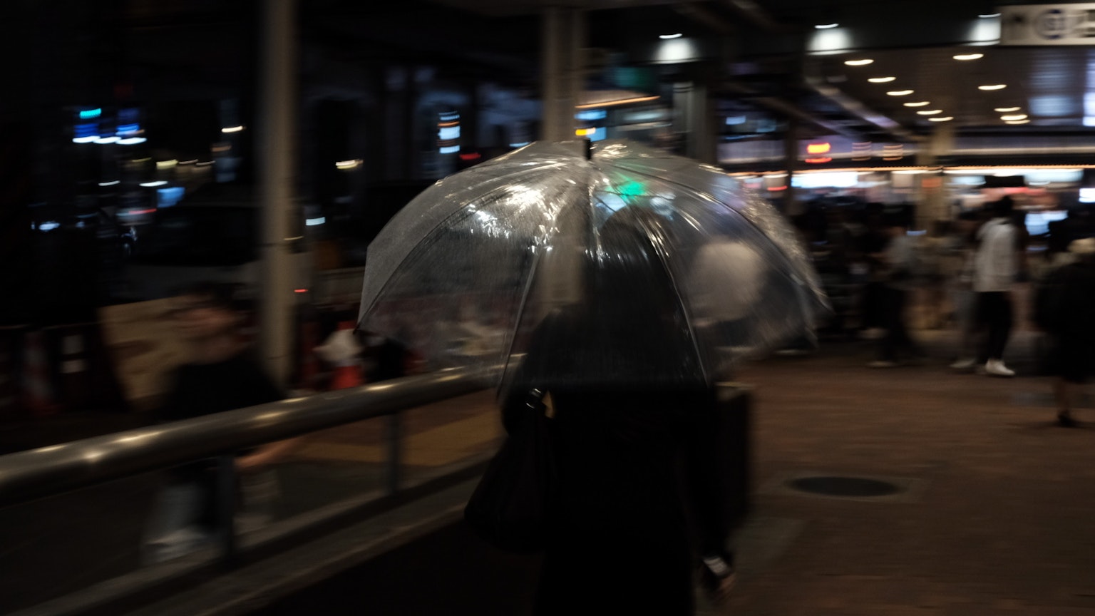 투명한 우산을 들고 혼잡한 지역을 걷는 사람의 밤 풍경