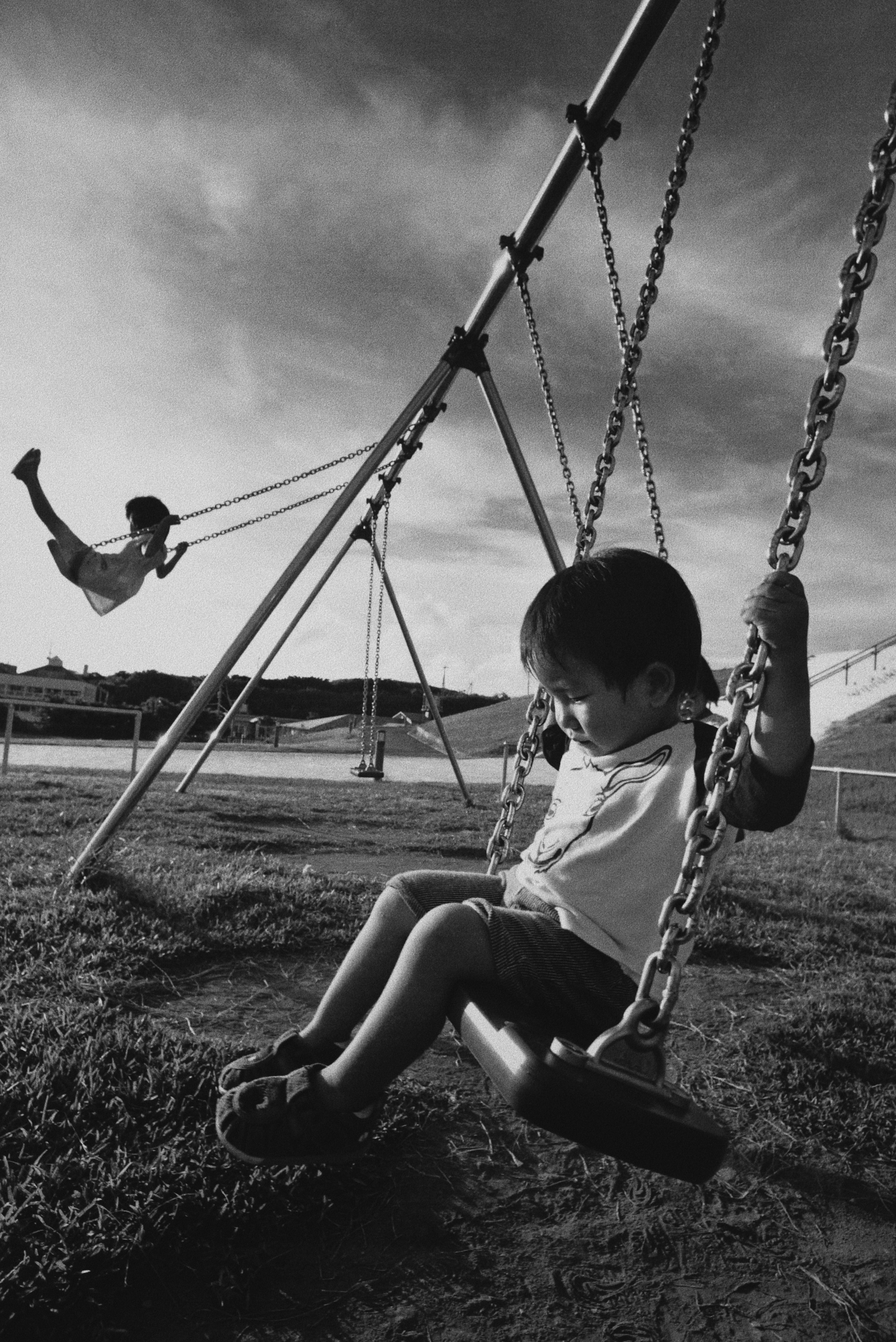 公園のブランコで遊ぶ子どもたちのモノクロ画像