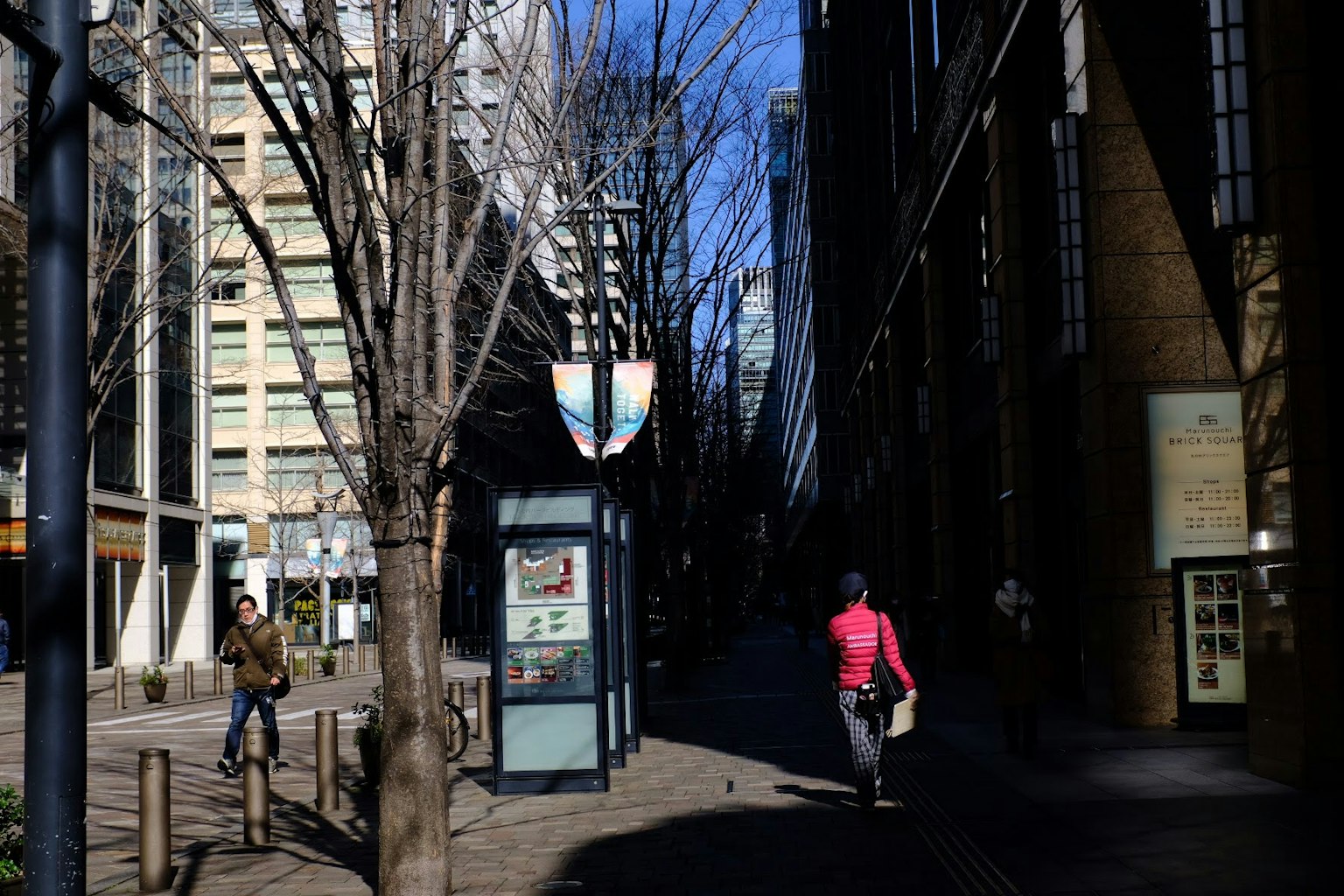 Scena urbana sotto un cielo blu con edifici e alberi una persona che cammina vicino a una fermata dell'autobus