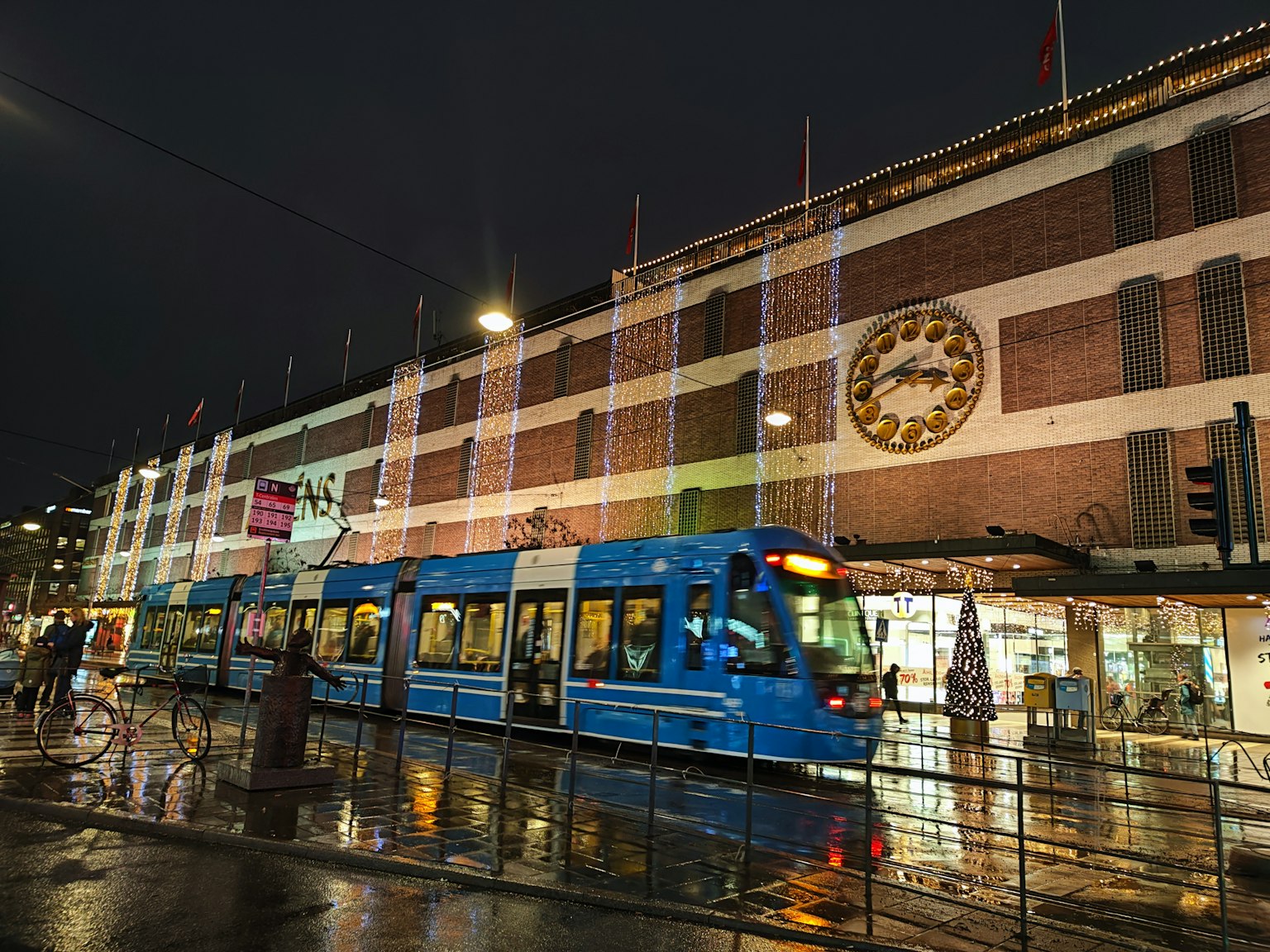 Blaues Straßenbahn fährt an einem hell erleuchteten Gebäude bei Nacht vorbei
