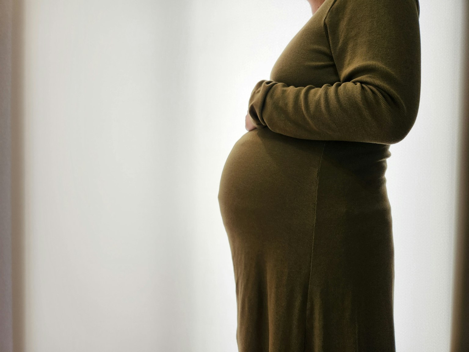 Silhouette of a pregnant woman in a green dress with hands on her belly
