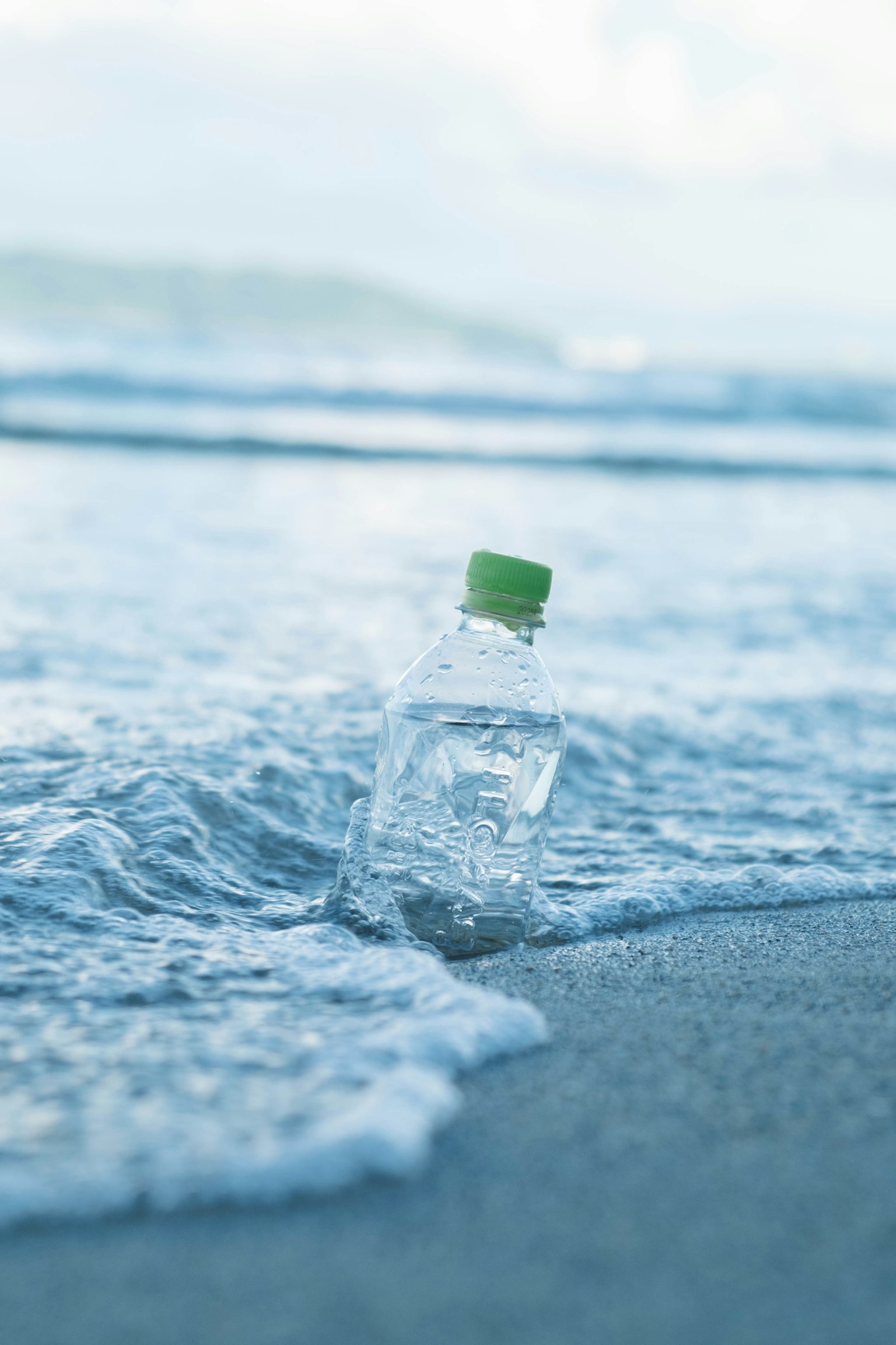 Botol air bening yang terdampar di pantai dengan ombak