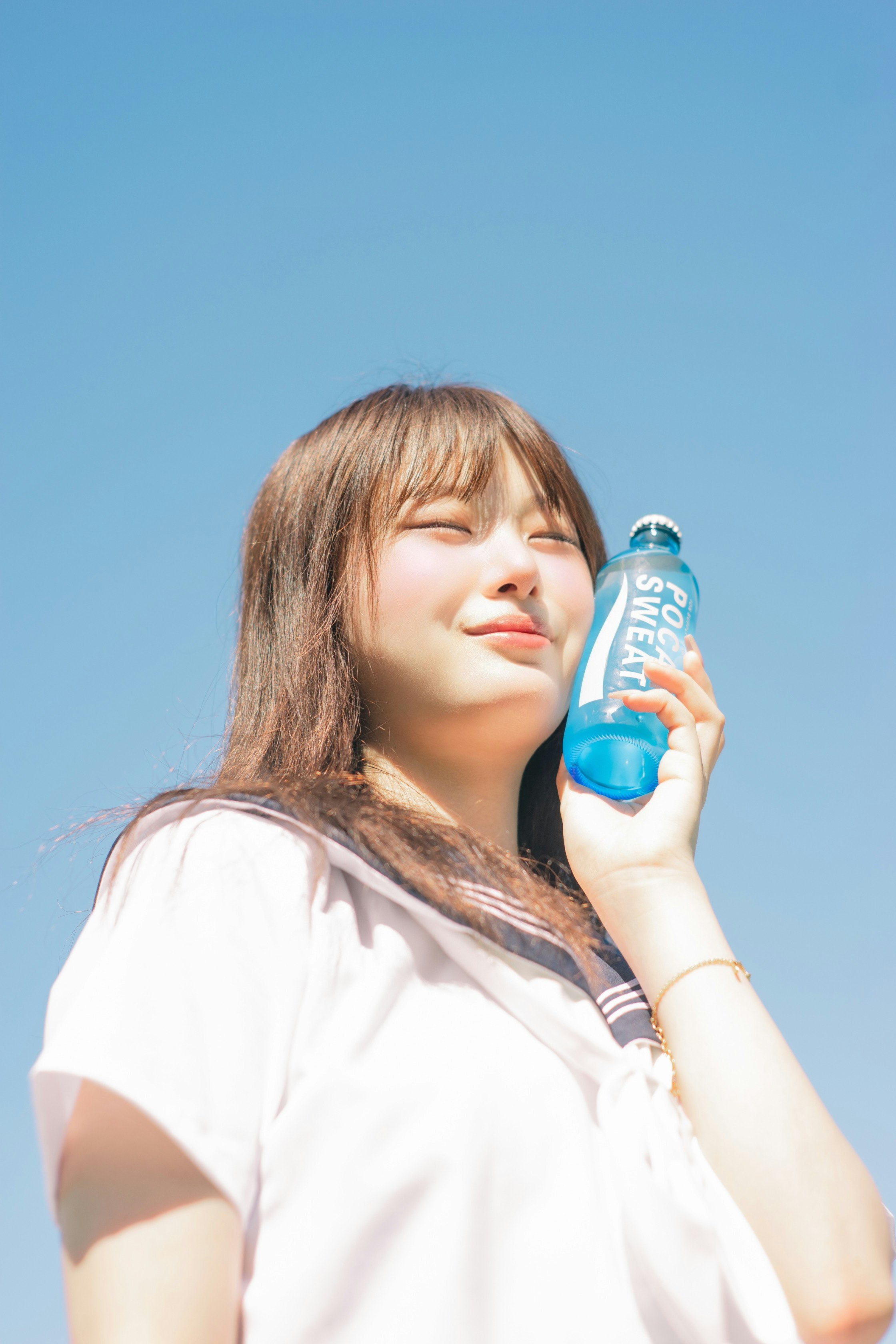 young woman smiling with a drink under a clear blue sky