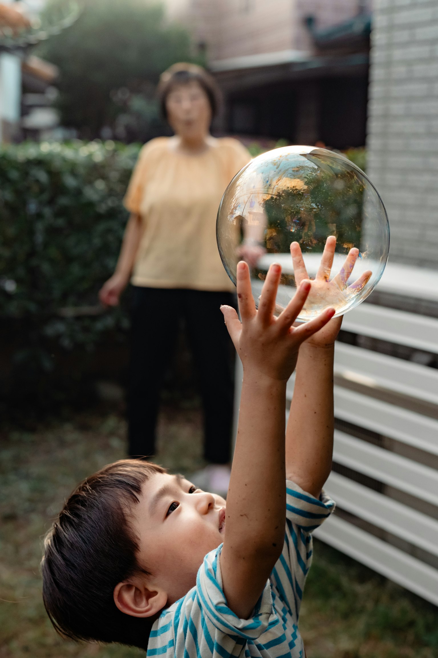 Un enfant atteignant une bulle de savon dans un jardin avec une femme adulte en arrière-plan