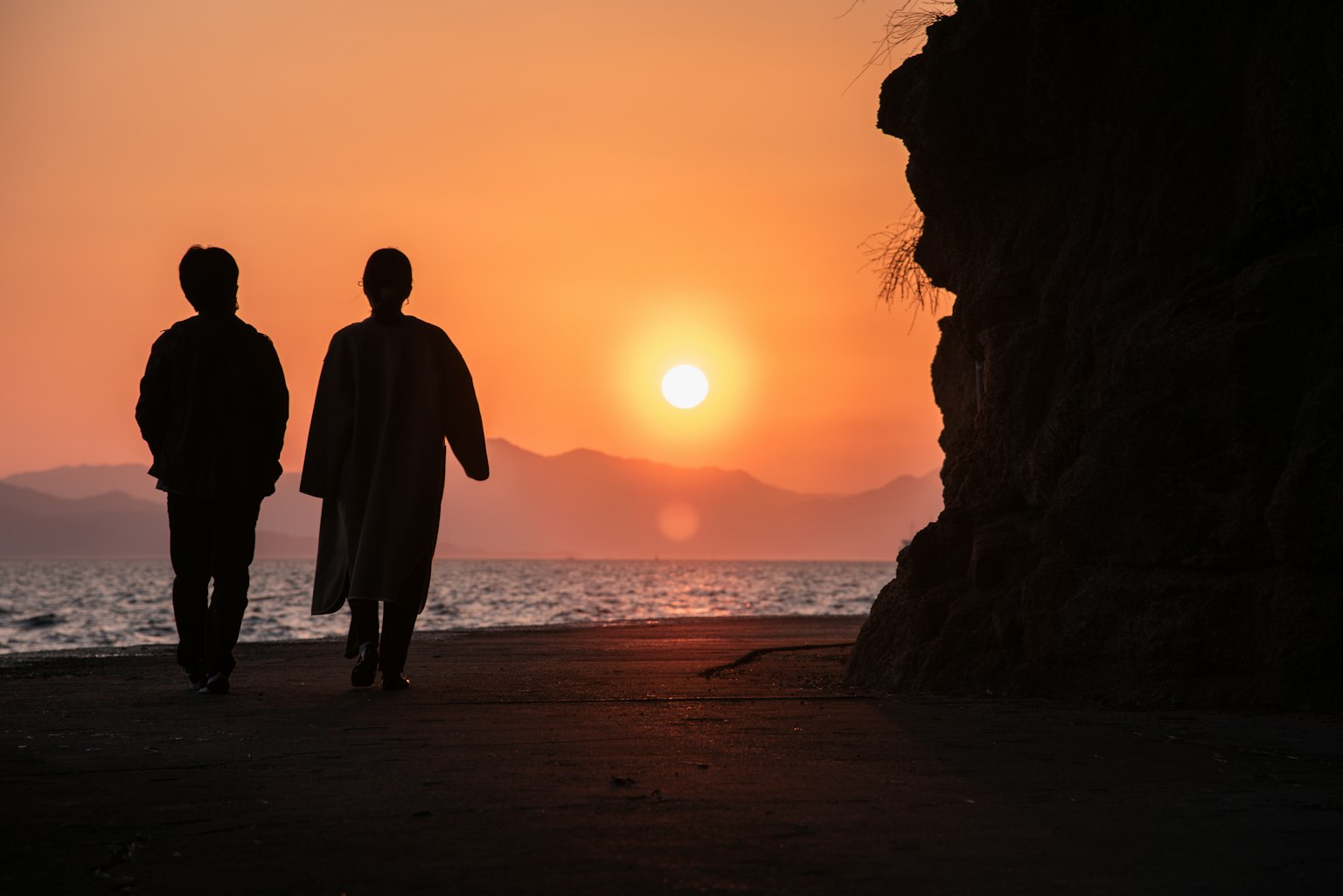 Silueta de dos personas caminando contra un fondo de atardecer Paisaje oceánico y montañoso