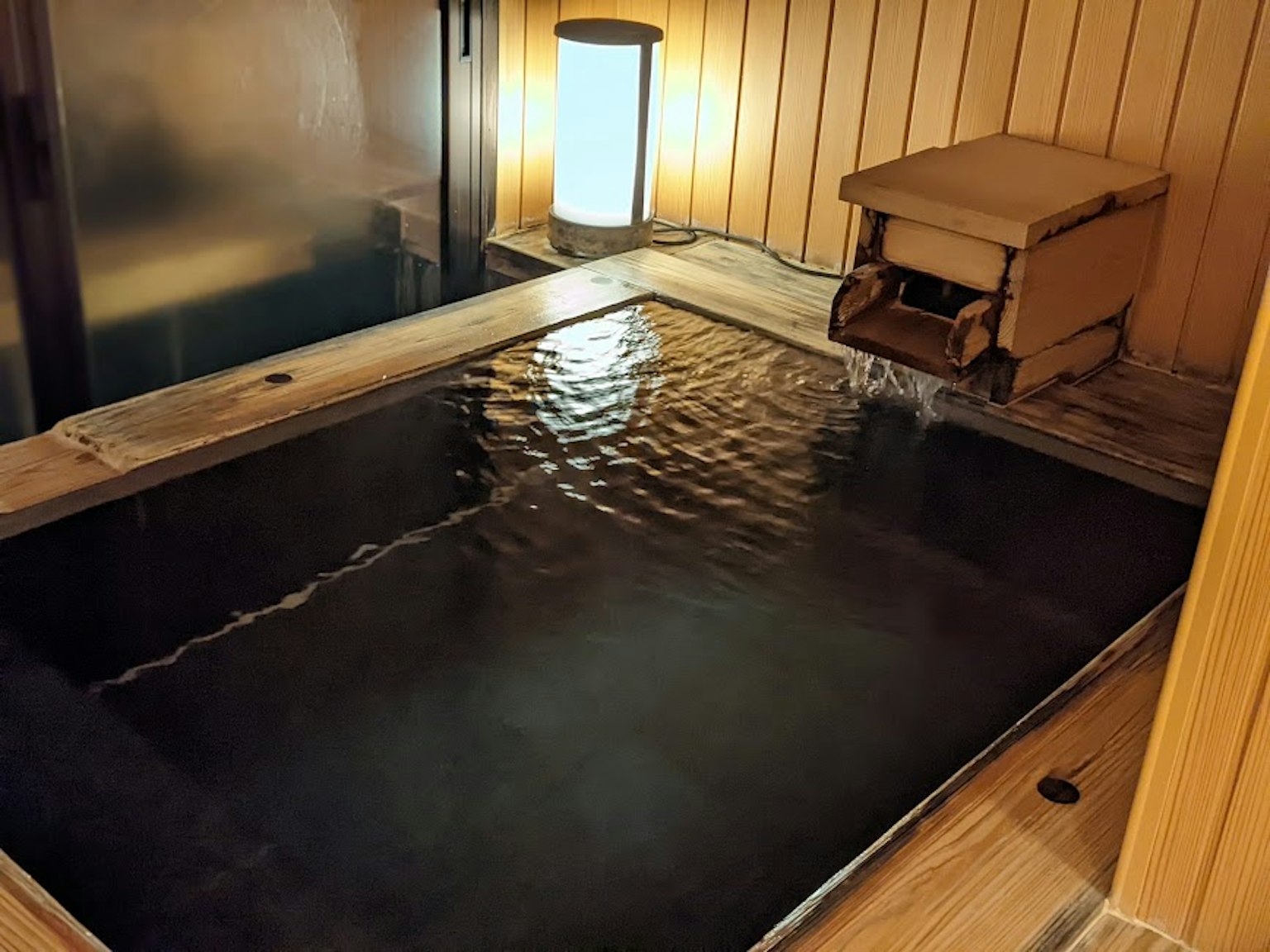 Holzbadewanne gefüllt mit warmem Wasser und eine sanft leuchtende Lampe