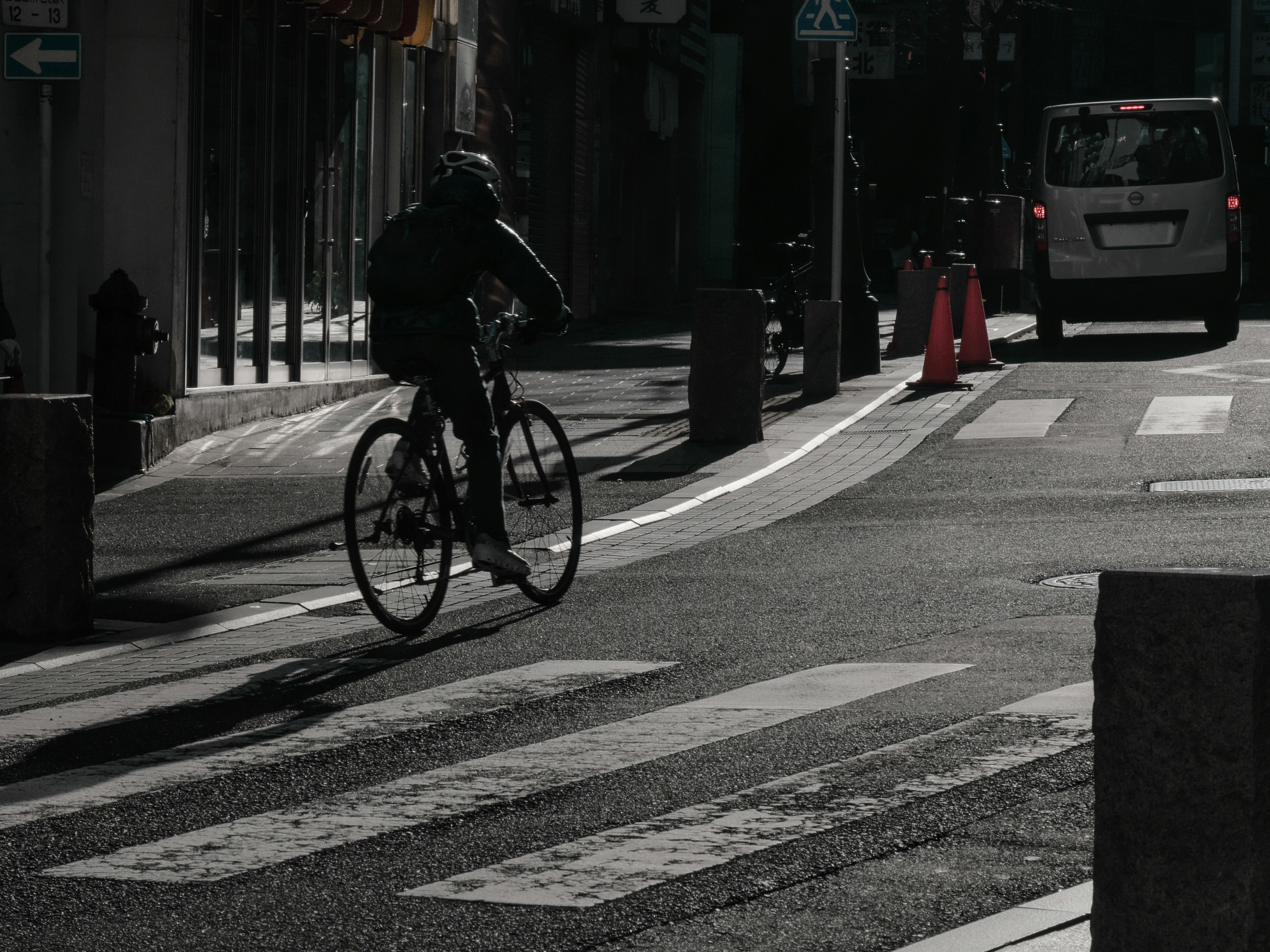 朝日を浴びる一ツ木通りを走り抜ける自転車のある横断歩道の街並み