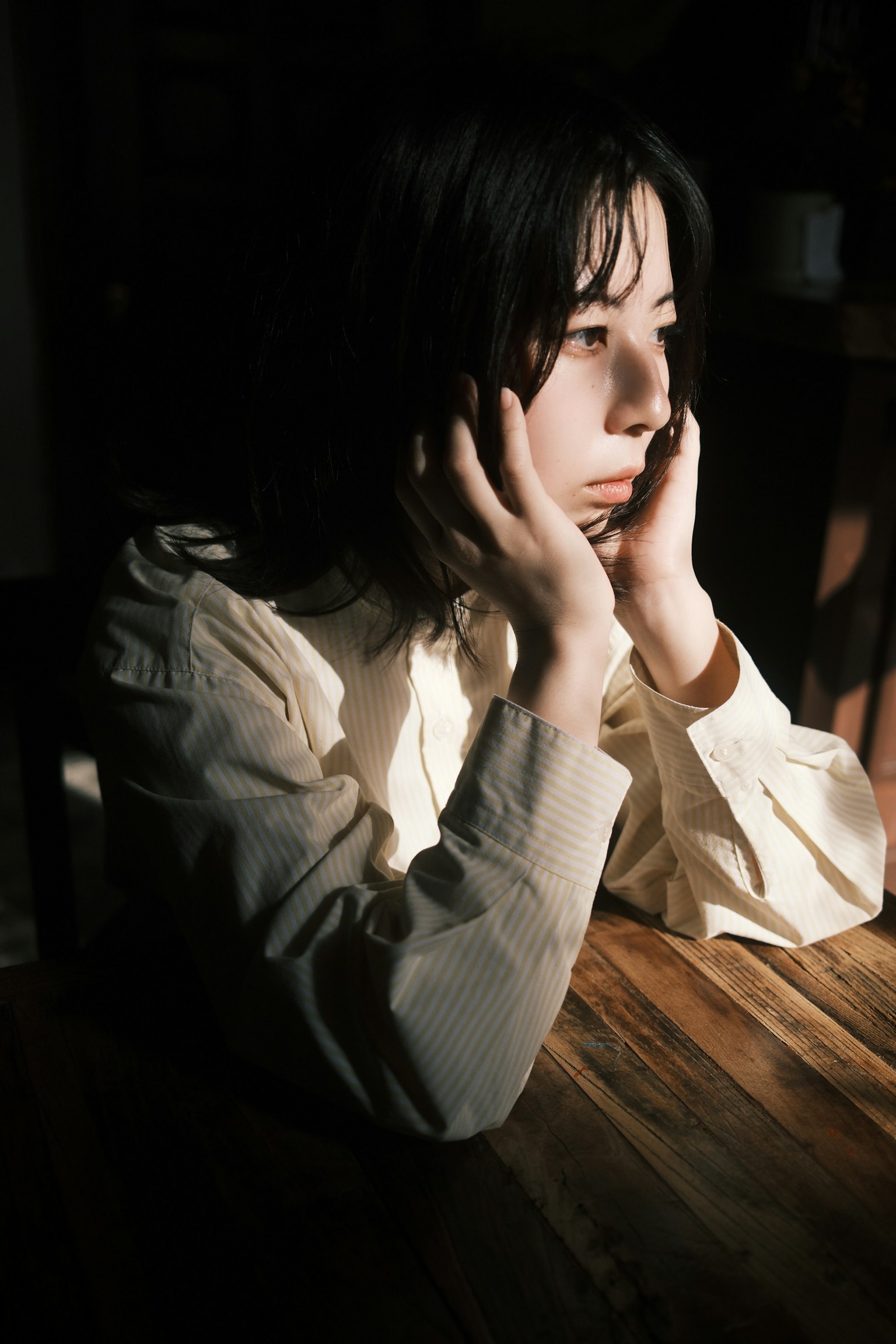 女性が木のテーブルに手を置いて考え込んでいる様子