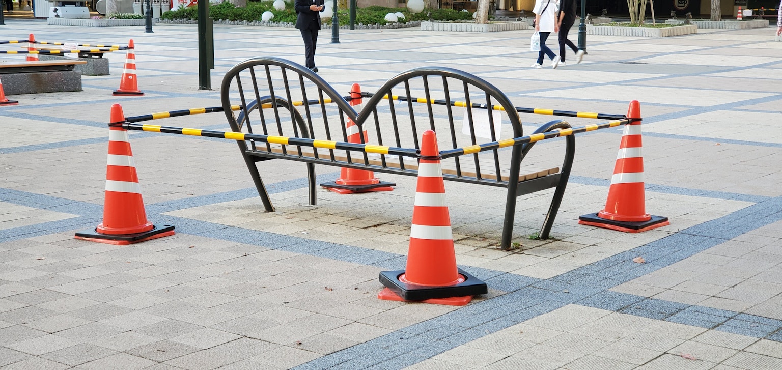 Eine Bank umgeben von gelb-schwarzer Absperrung mit Verkehrshütchen auf einem öffentlichen Platz