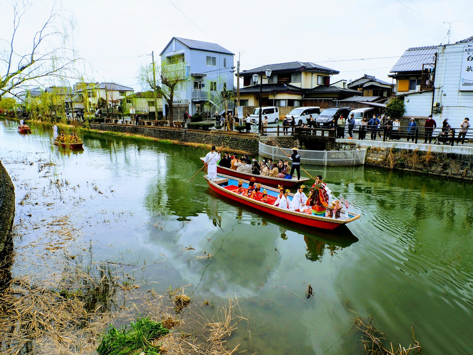 Perahu tradisional berlayar di sungai dengan rumah-rumah di tepi