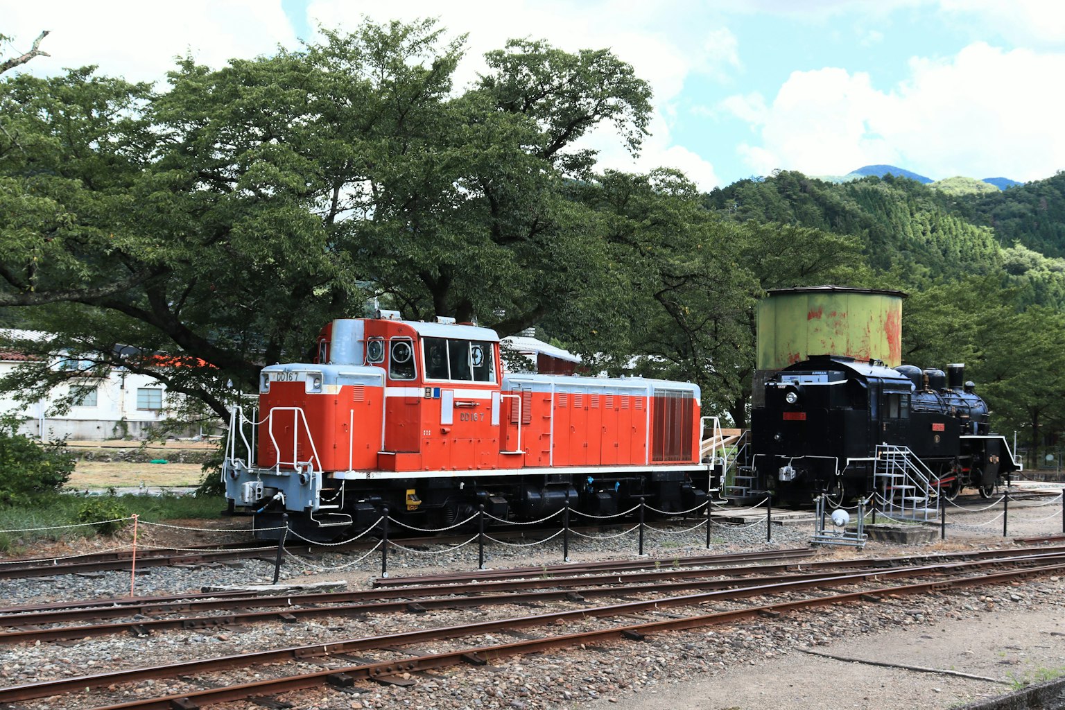 รถไฟดีเซลสีส้มและรถไฟไอน้ำสีดำอยู่ข้างกัน