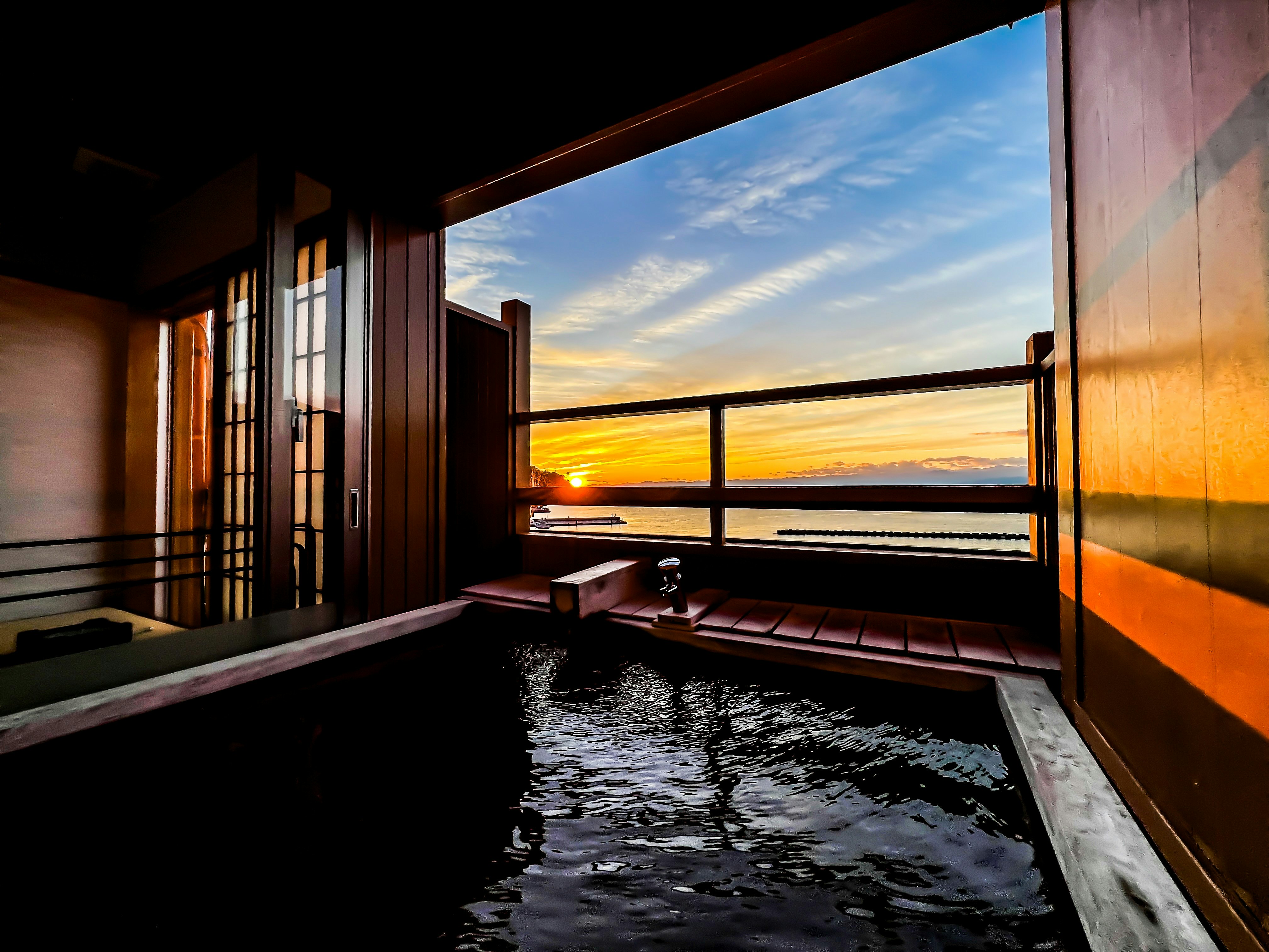 Chambre japonaise avec bain en plein air donnant sur la mer au coucher du soleil
