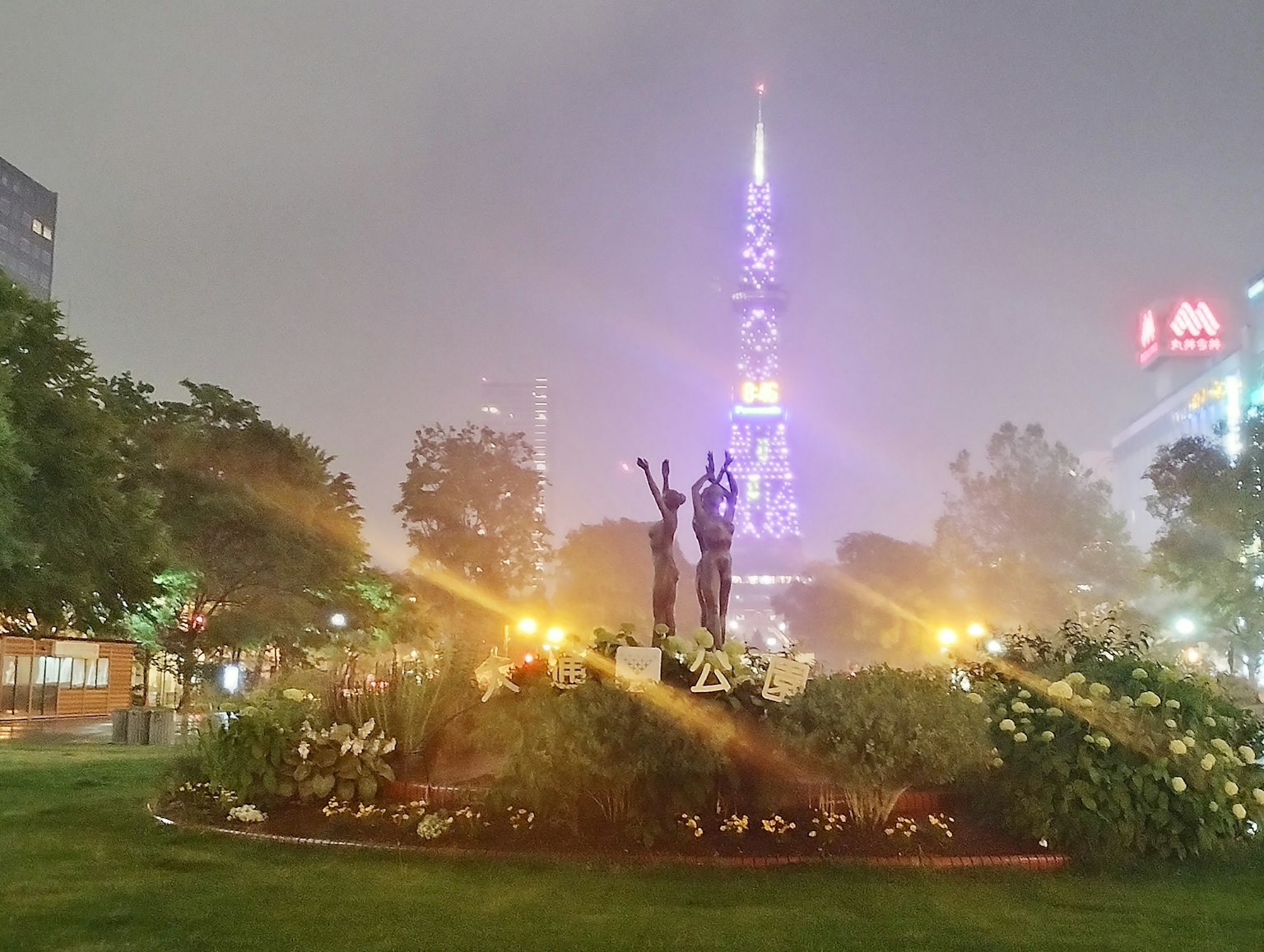 Vista nocturna de un parque con una torre y esculturas
