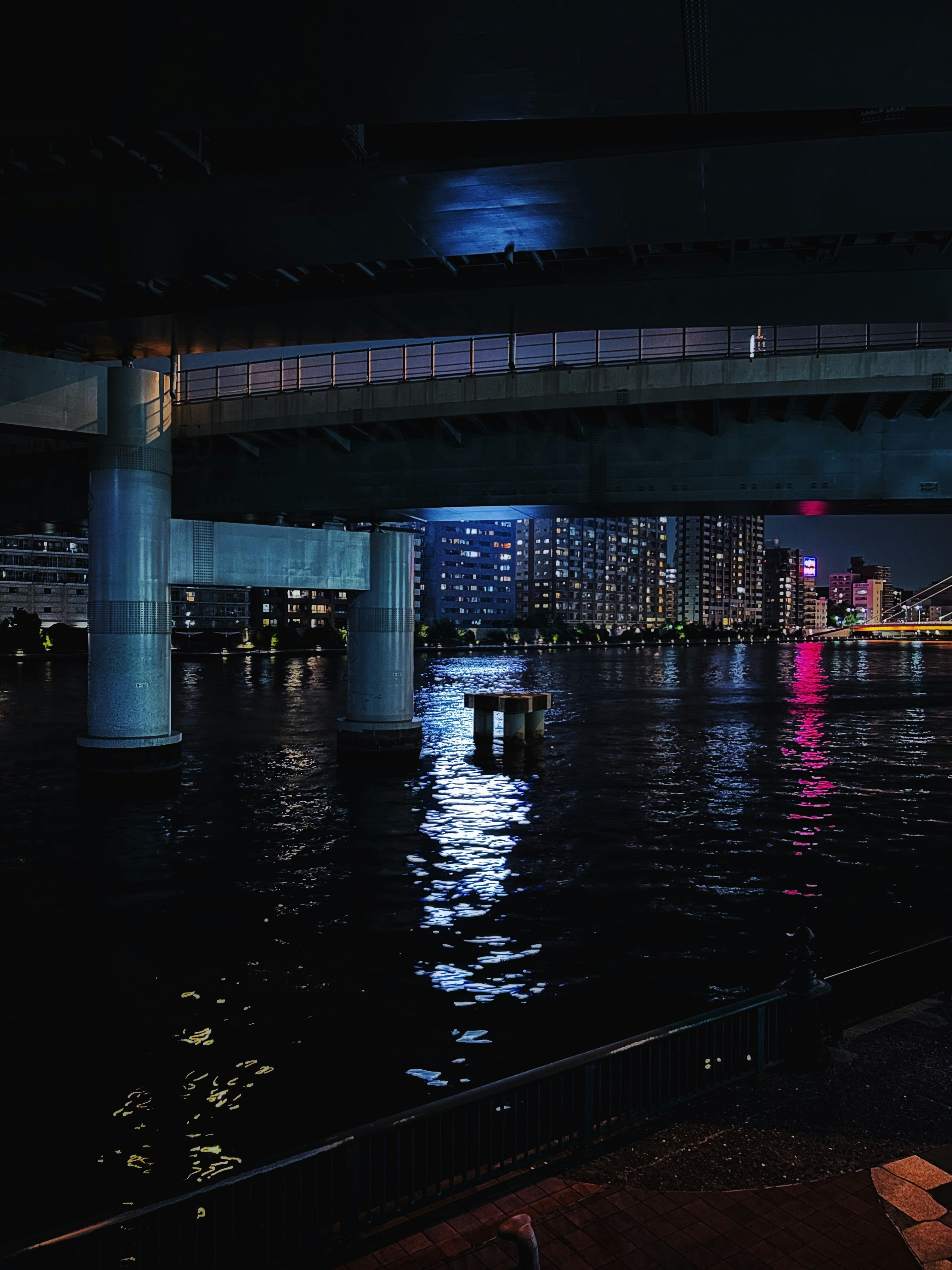 pont de nuit au-dessus d’une rivière avec reflets néon des immeubles