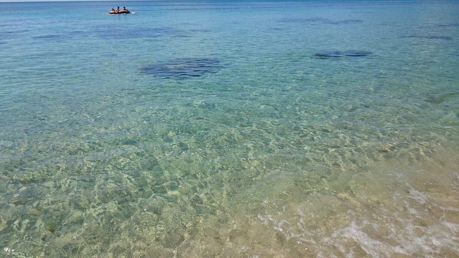 Acqua turchese trasparente con fondale visibile e una barca in lontananza