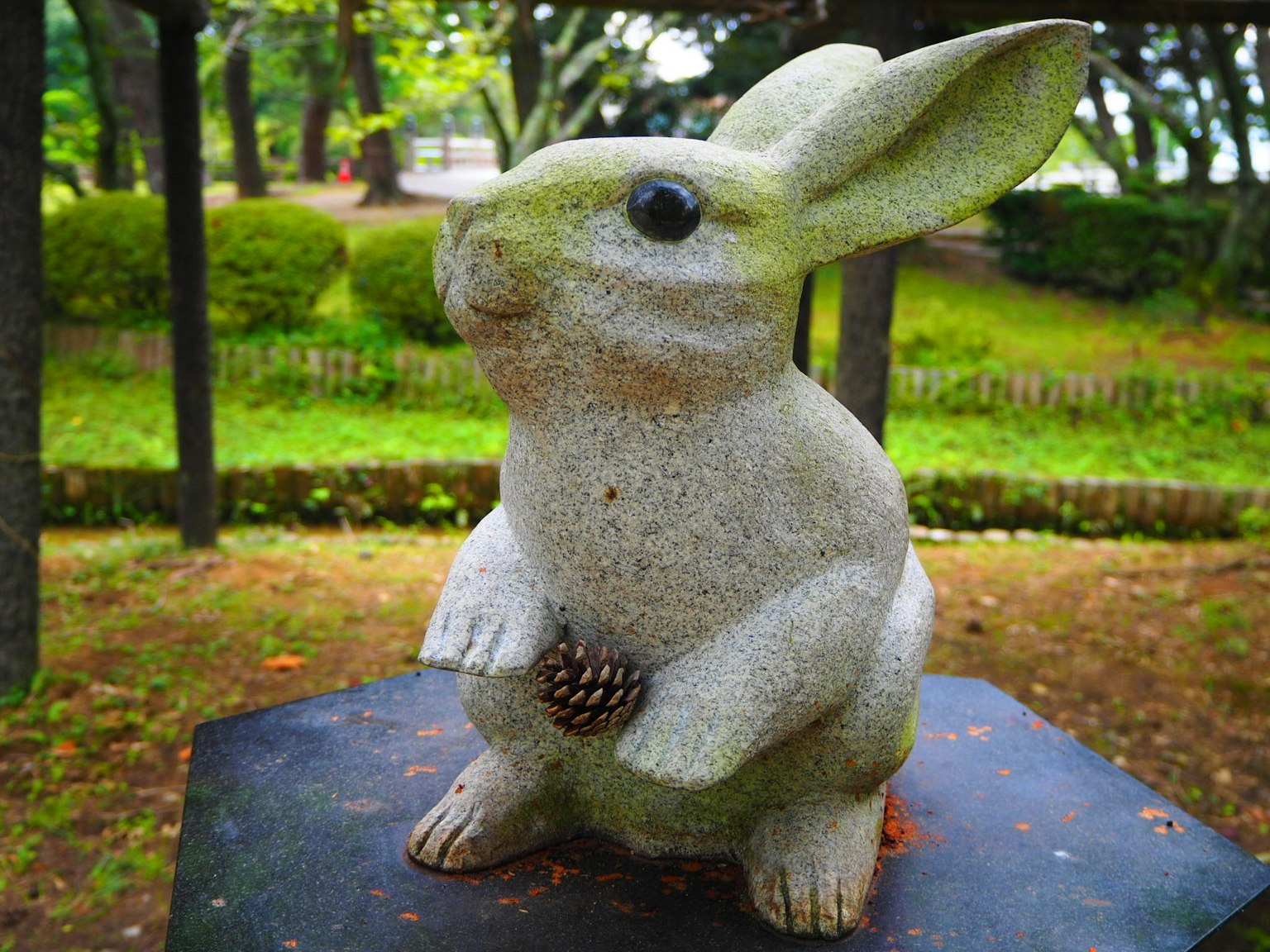 Patung kelinci lucu di taman yang memegang kerucut pinus