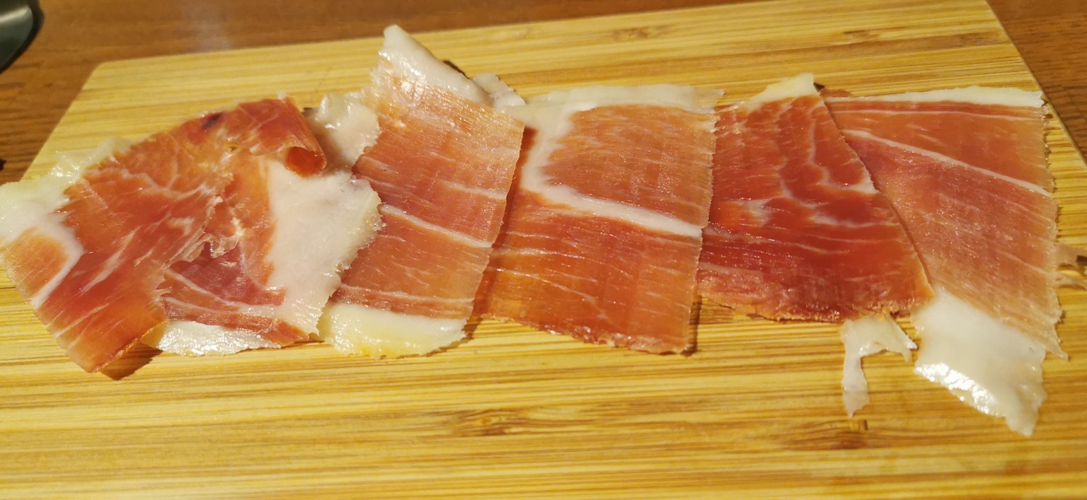 Irisan tipis Jamón Ibérico disusun di atas papan kayu