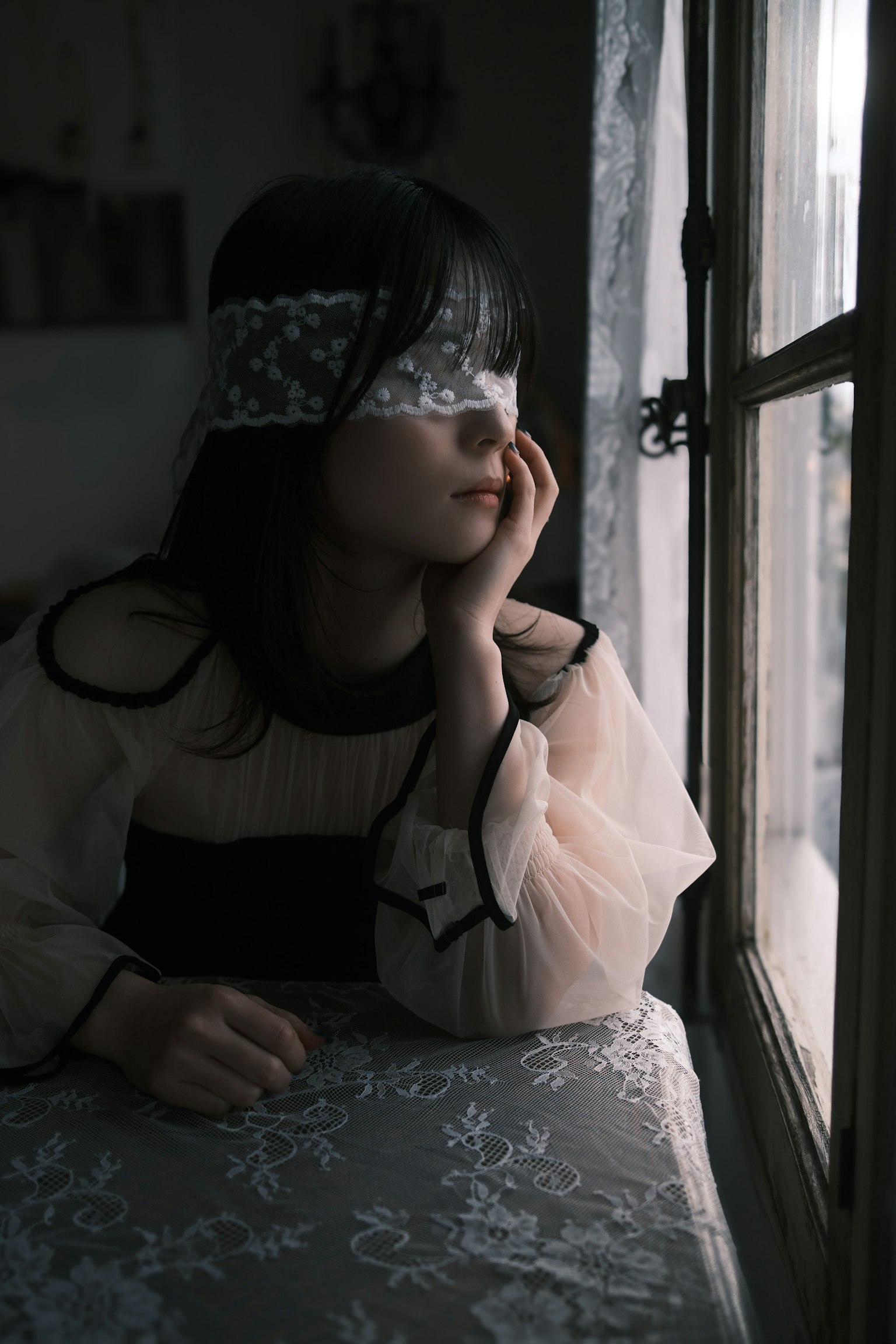 窓の外を見つめる少女 黒と白のドレスを着ている 目を隠すレースのバンドを着用