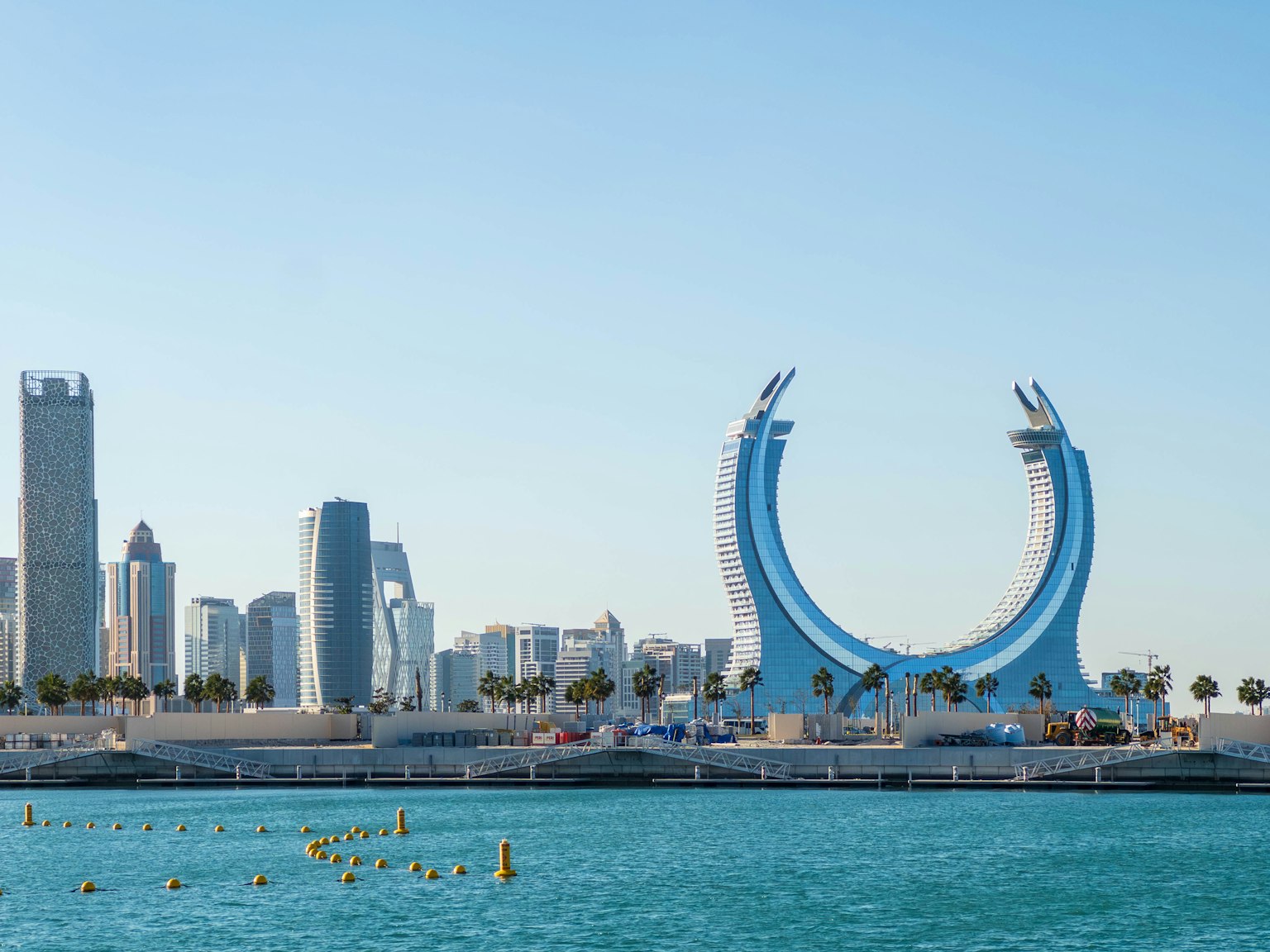 Lengkungan ikonik di Qatar dengan laut biru dan bangunan modern di latar belakang