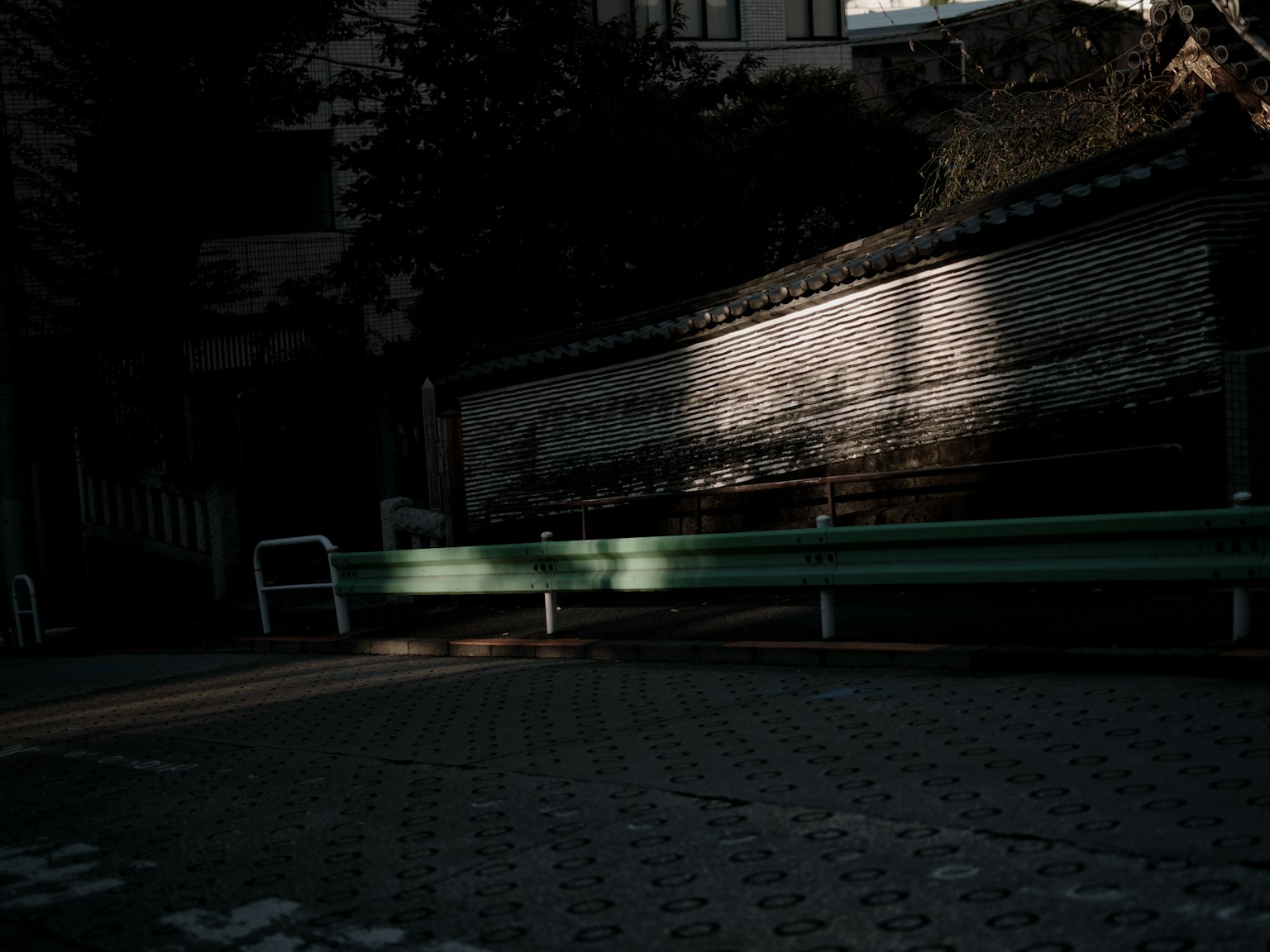 Une scène tranquille avec un banc vert sur fond sombre et une partie d'un mur visible