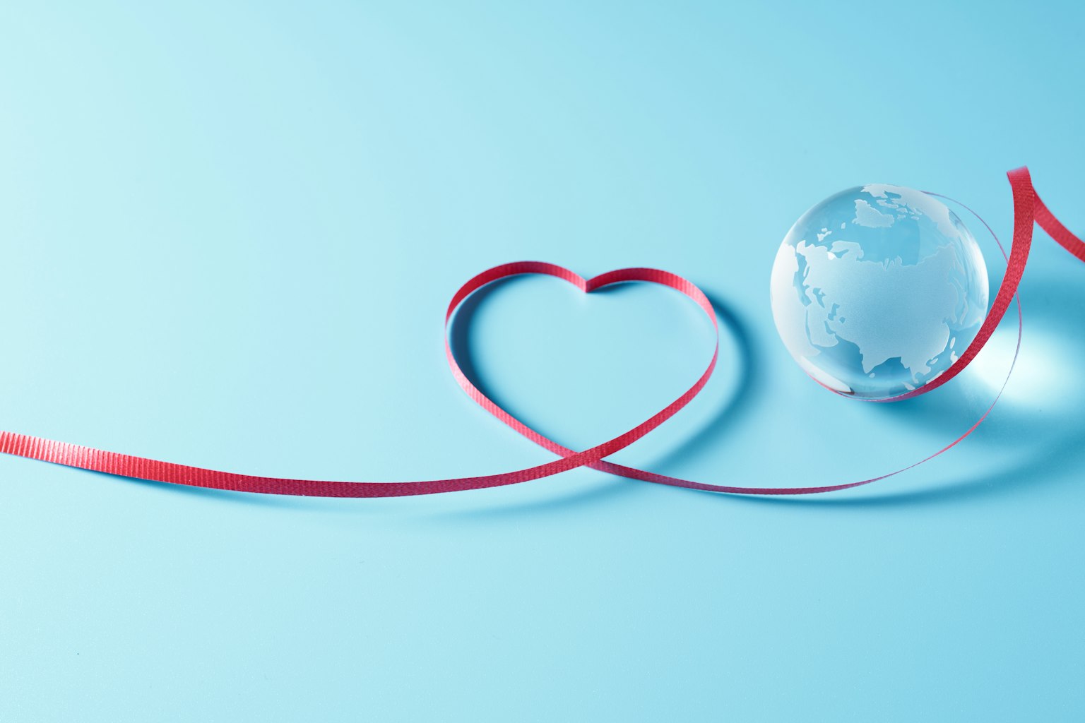 Un nastro rosso a forma di cuore e un globo trasparente su uno sfondo azzurro