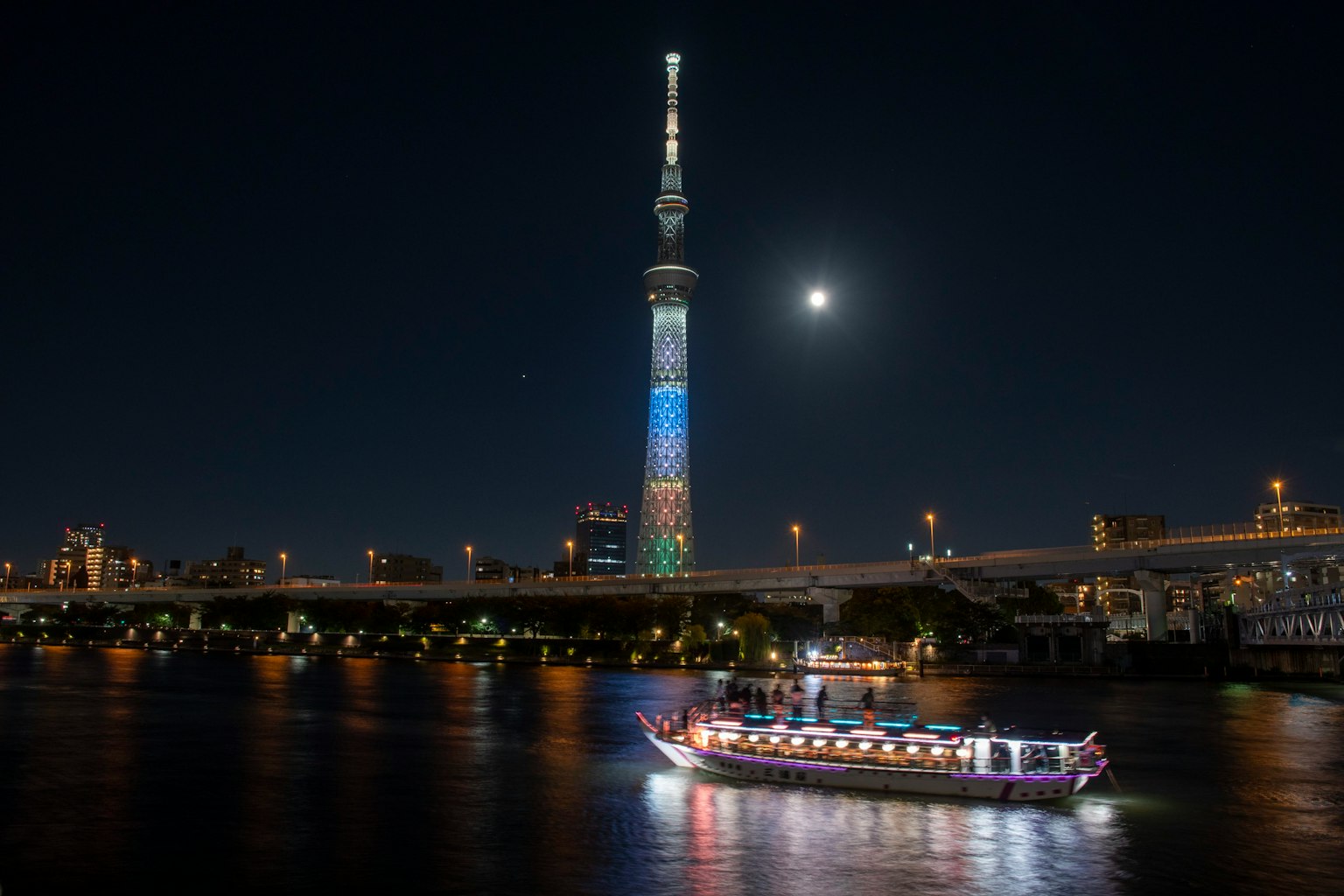 Tokyo Skytree nachts beleuchtet mit einem Boot auf dem Fluss