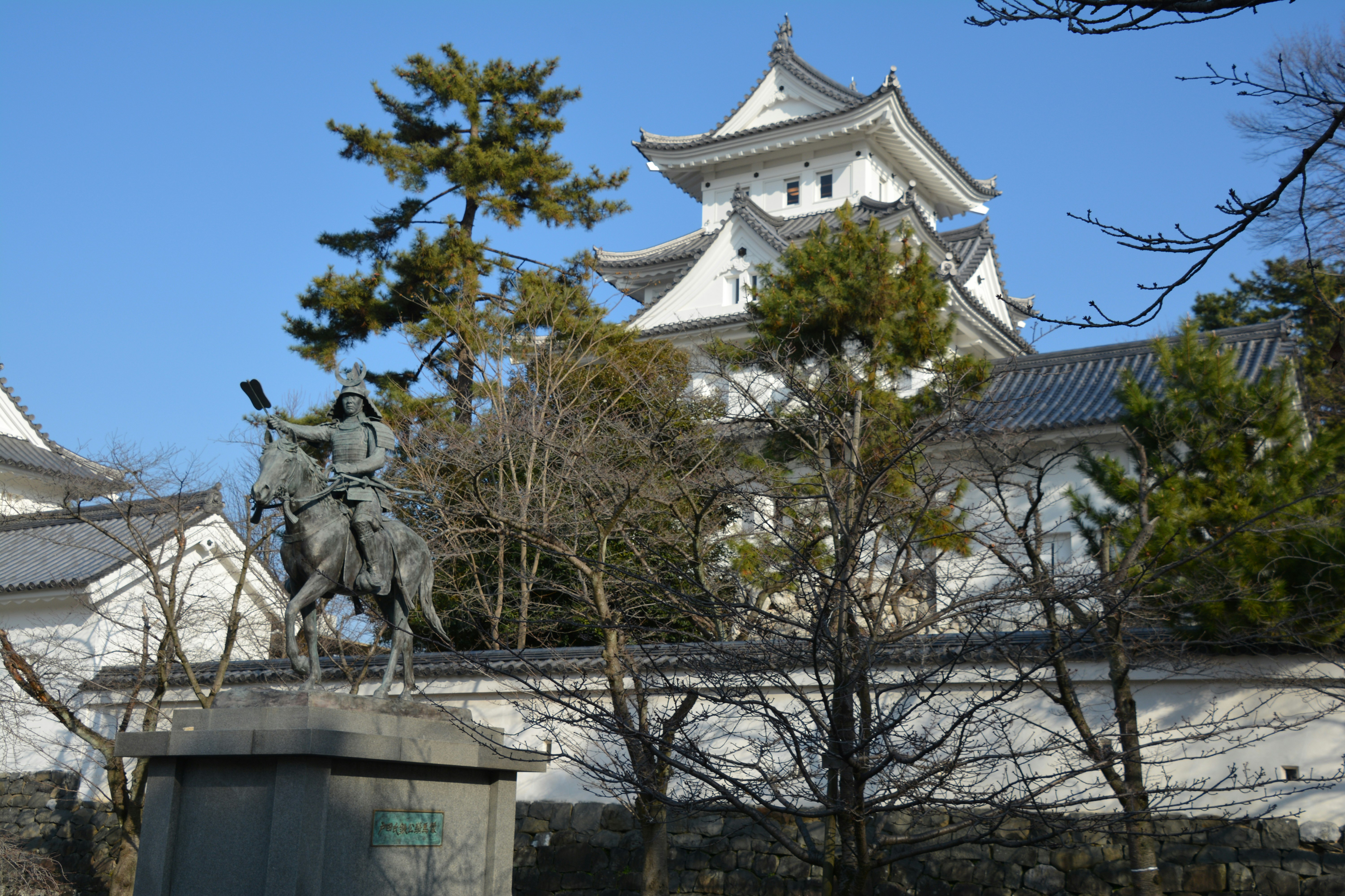 馬に乗る武将像と城郭の天守が見える城跡