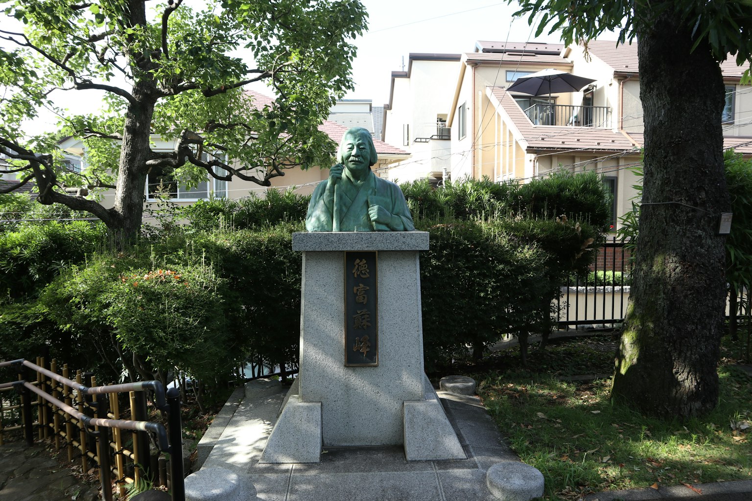 Bronze statue in a green garden setting with surrounding houses